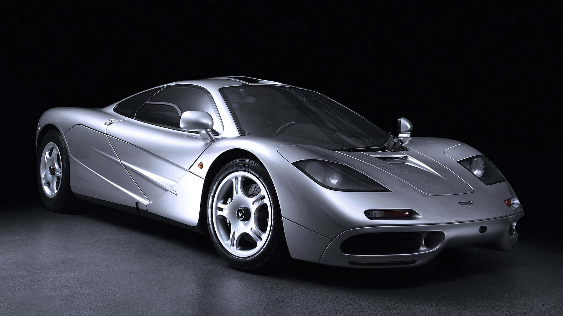 Mclaren F1 桌布 壁紙 — 一輛時尚的銀色McLaren F1超級跑車在攝影棚燈光下閃閃發光，背景為黑色，地板具有反射效果。