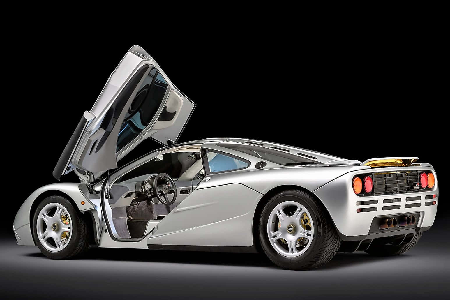 Mclaren F1 桌布 壁紙 — 一架流線型銀色McLaren F1超級跑車，鷗翼車門打開，襯托黑色工作室背景。