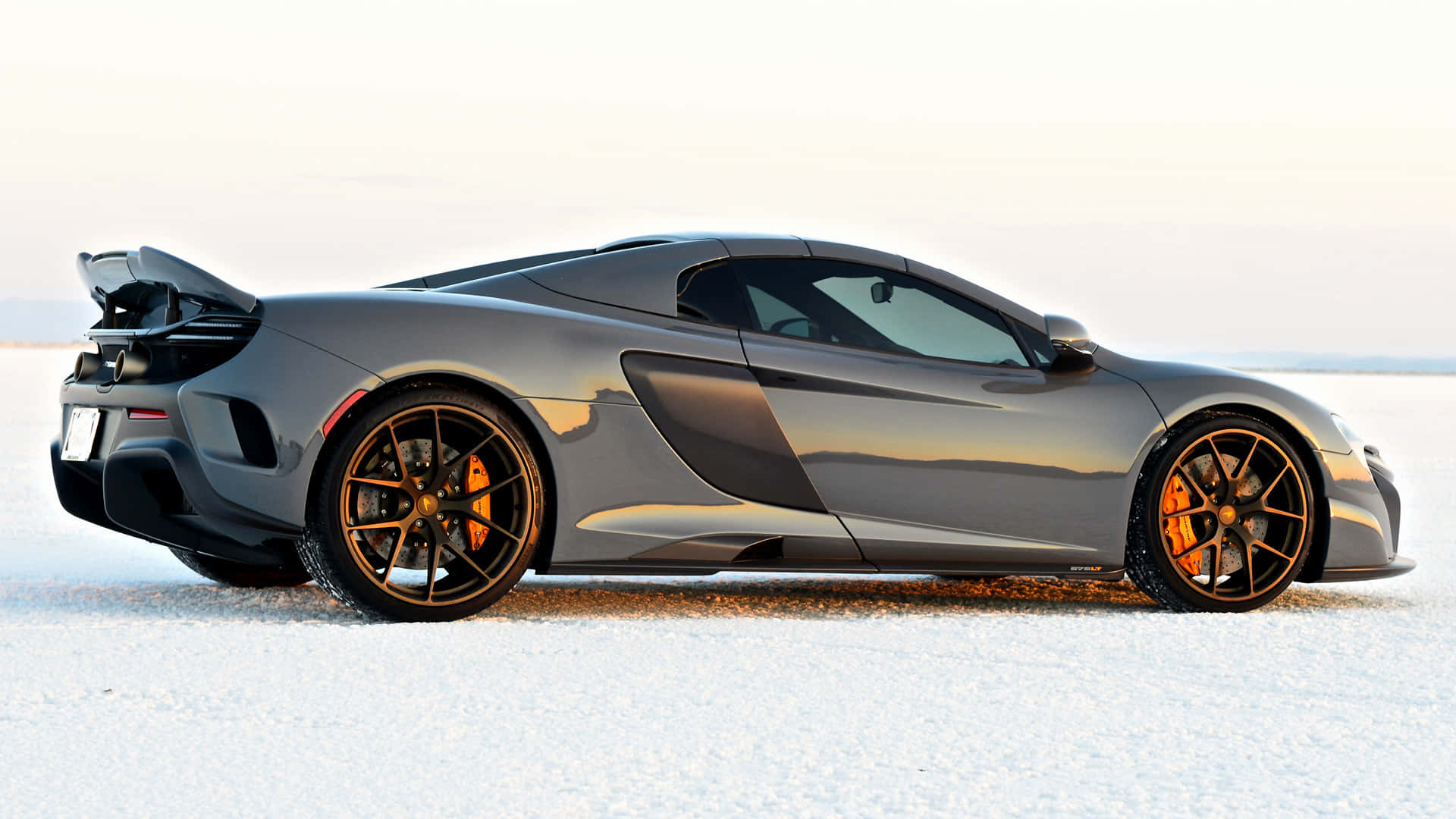 Mclaren 675lt Spider 桌布 壁紙 — 一輛流線型銀色McLaren跑車配金色輪圈，停泊在廣闊的白色鹽灘上，天空明亮。