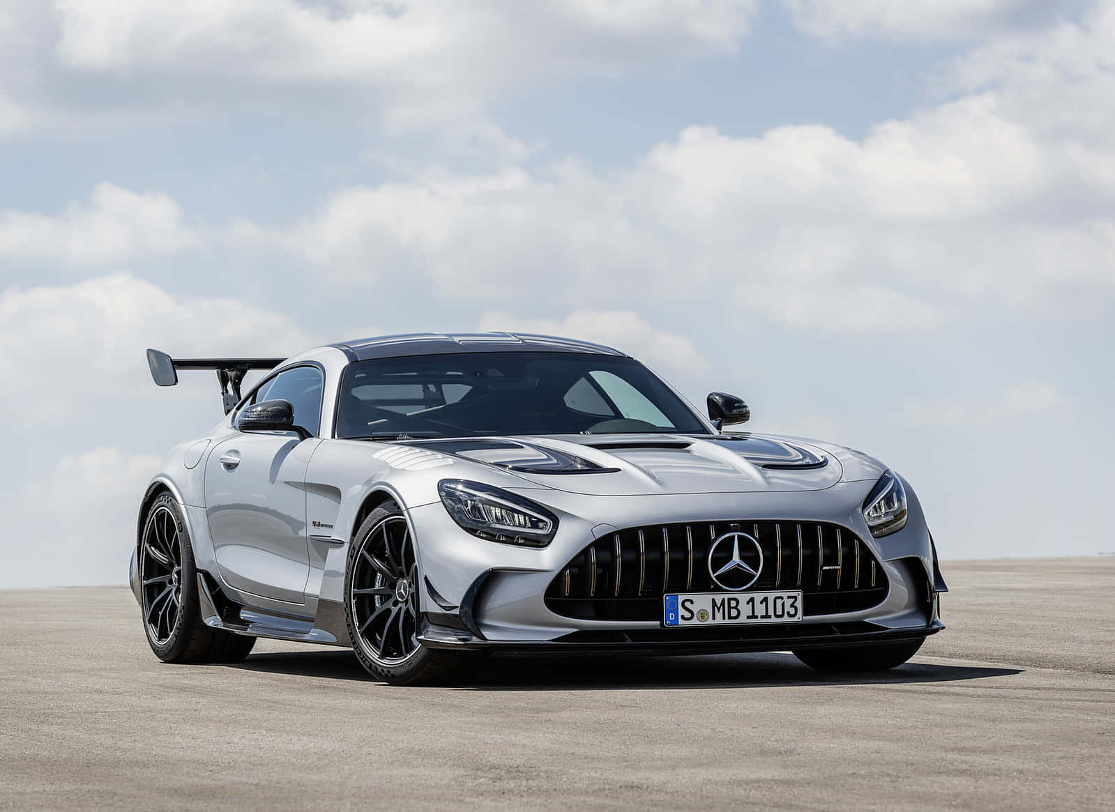 Mercedes Benz Amg Gt 桌布 壁紙 — 一輛時尚的銀色 Mercedes-AMG GT Black Series 跑車，配備黑色車輪和後擾流板，停放在廣闊的露天瀝青地面上，天空部分多雲。