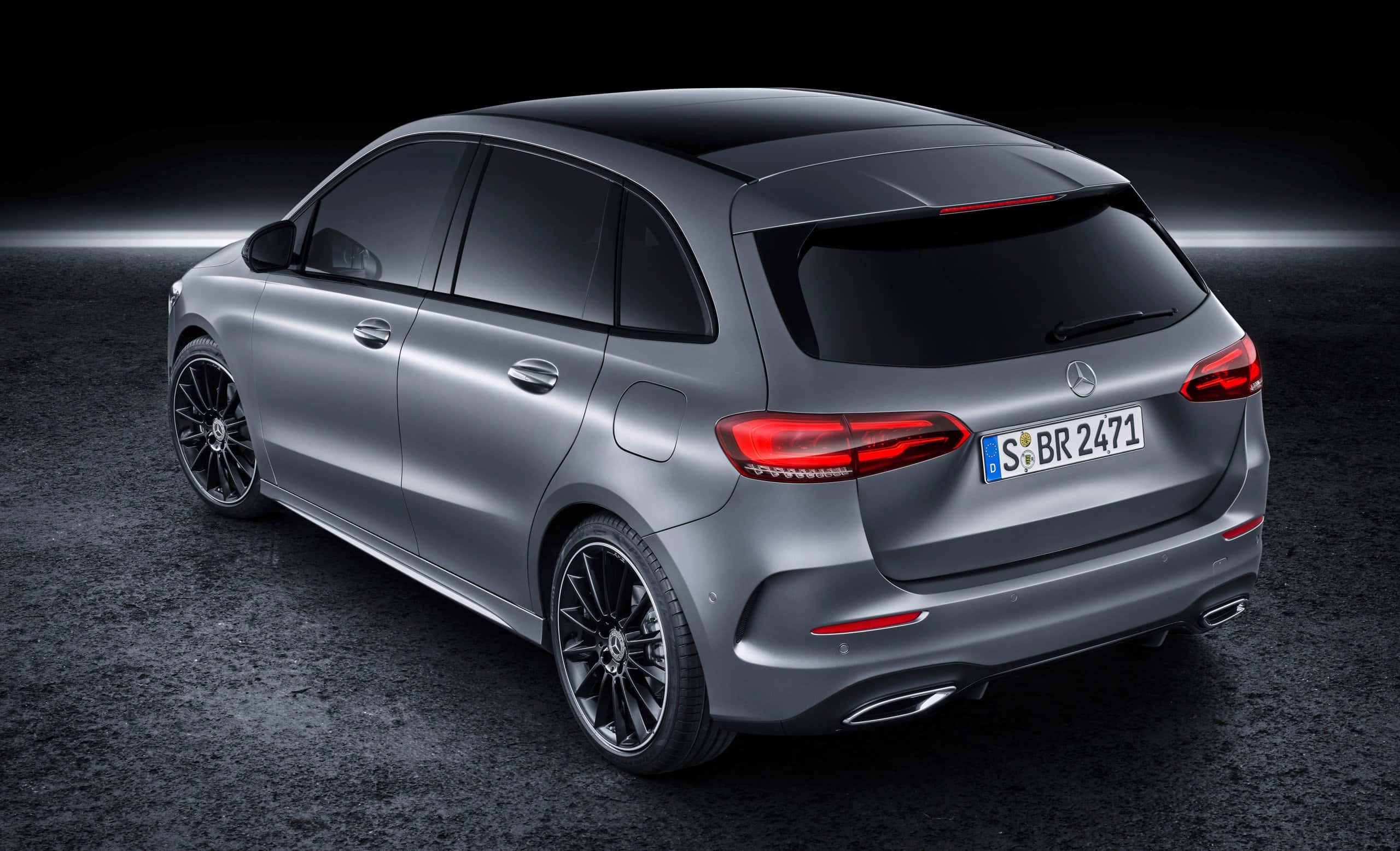 Mercedes Benz B-class 桌布 壁紙 — 一輛時尚的銀色梅賽德斯-奔馳旅行車，配備黑色輪圈和發光的紅色尾燈，在戲劇性的工作室燈光下停在深色紋理表面上。