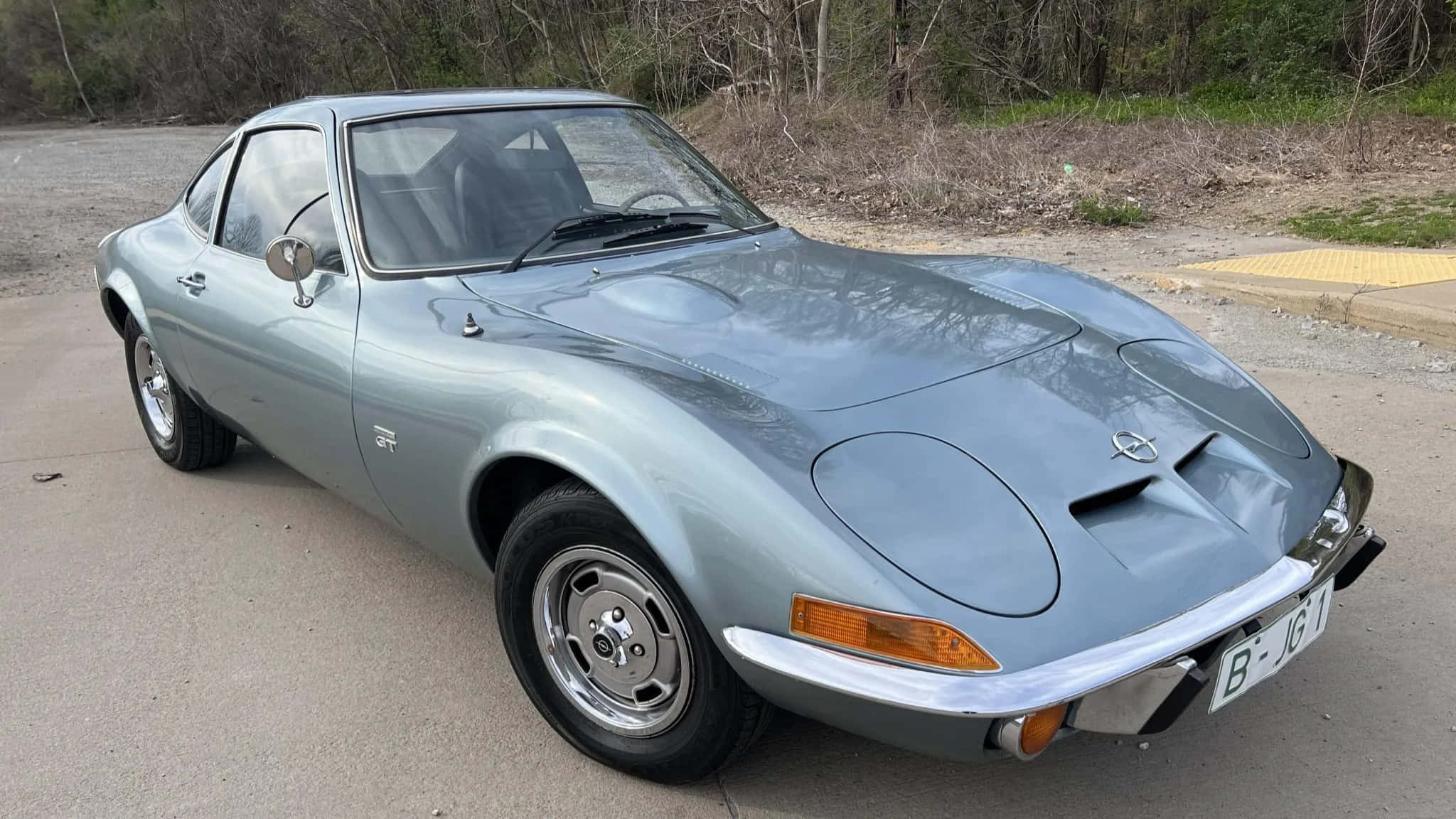 Opel Gt 桌布 壁紙 — 一輛時尚的銀色歐寶GT跑車停放在混凝土場地上，背景有乾燥灌木和樹木。