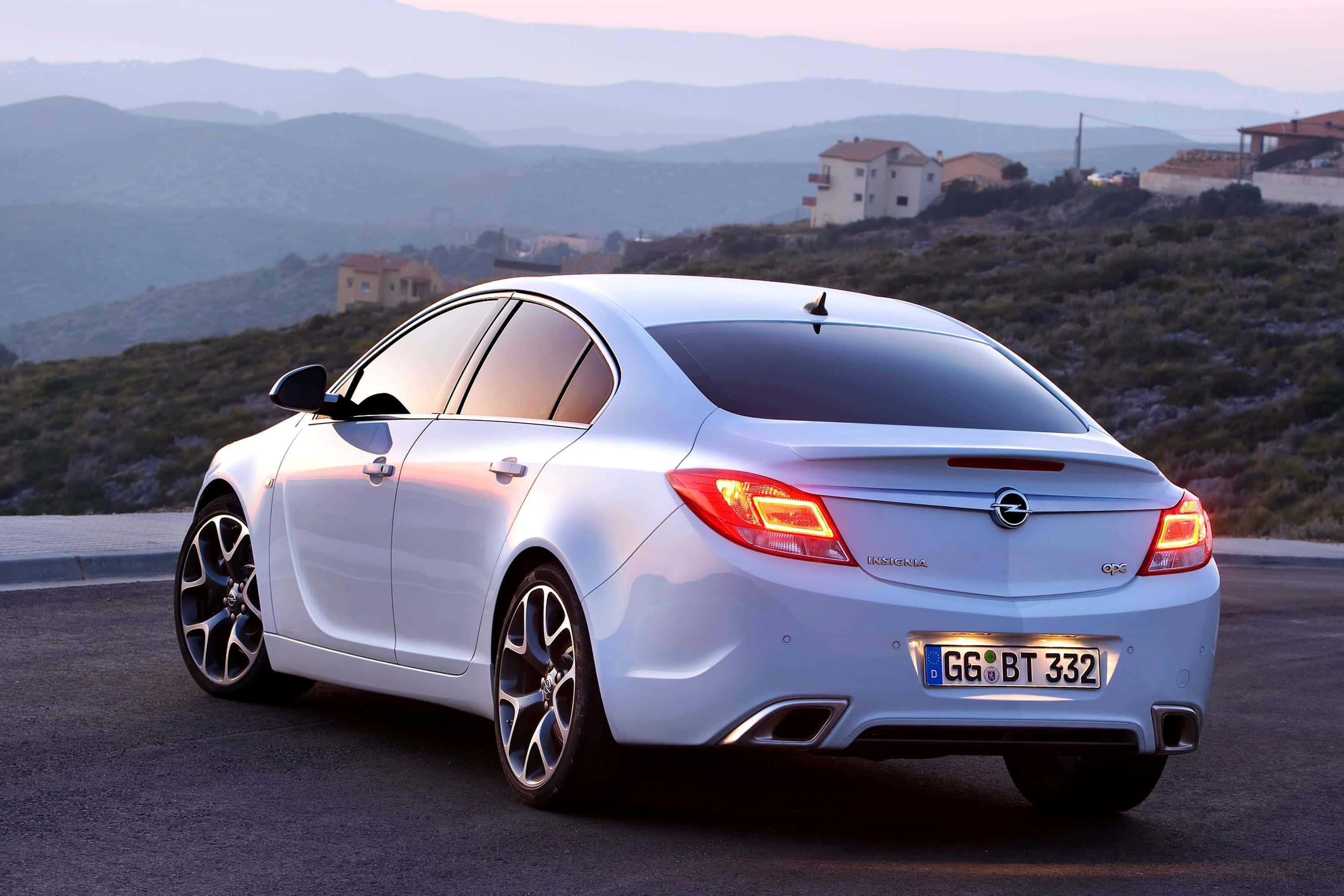 Opel Insignia 桌布 壁紙 — 一架流線型銀色Opel Insignia GTC停泊在日落時分的沿海公路上，背景是起伏的山丘和房屋。