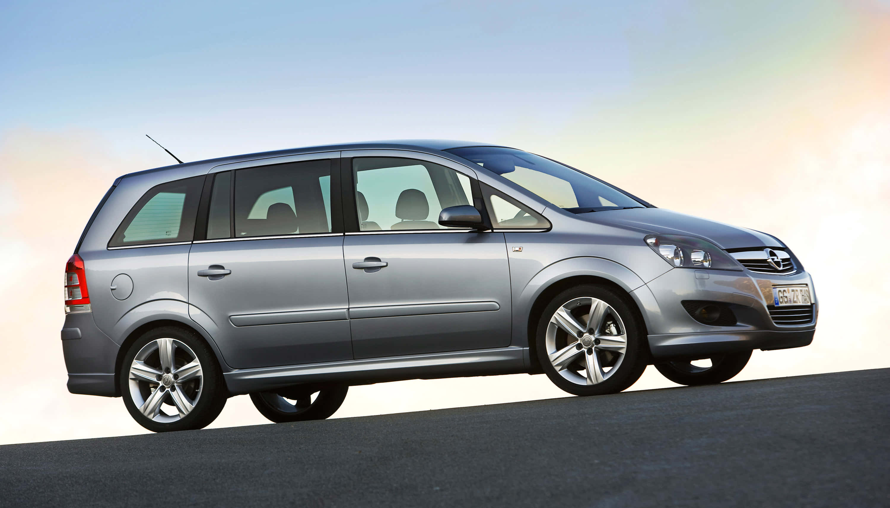 Opel Zafira 桌布 壁紙 — 一輛時尚的銀色Opel Zafira旅行車停在柏油路上，天空呈現柔和漸層色，帶有溫暖的日出色調。