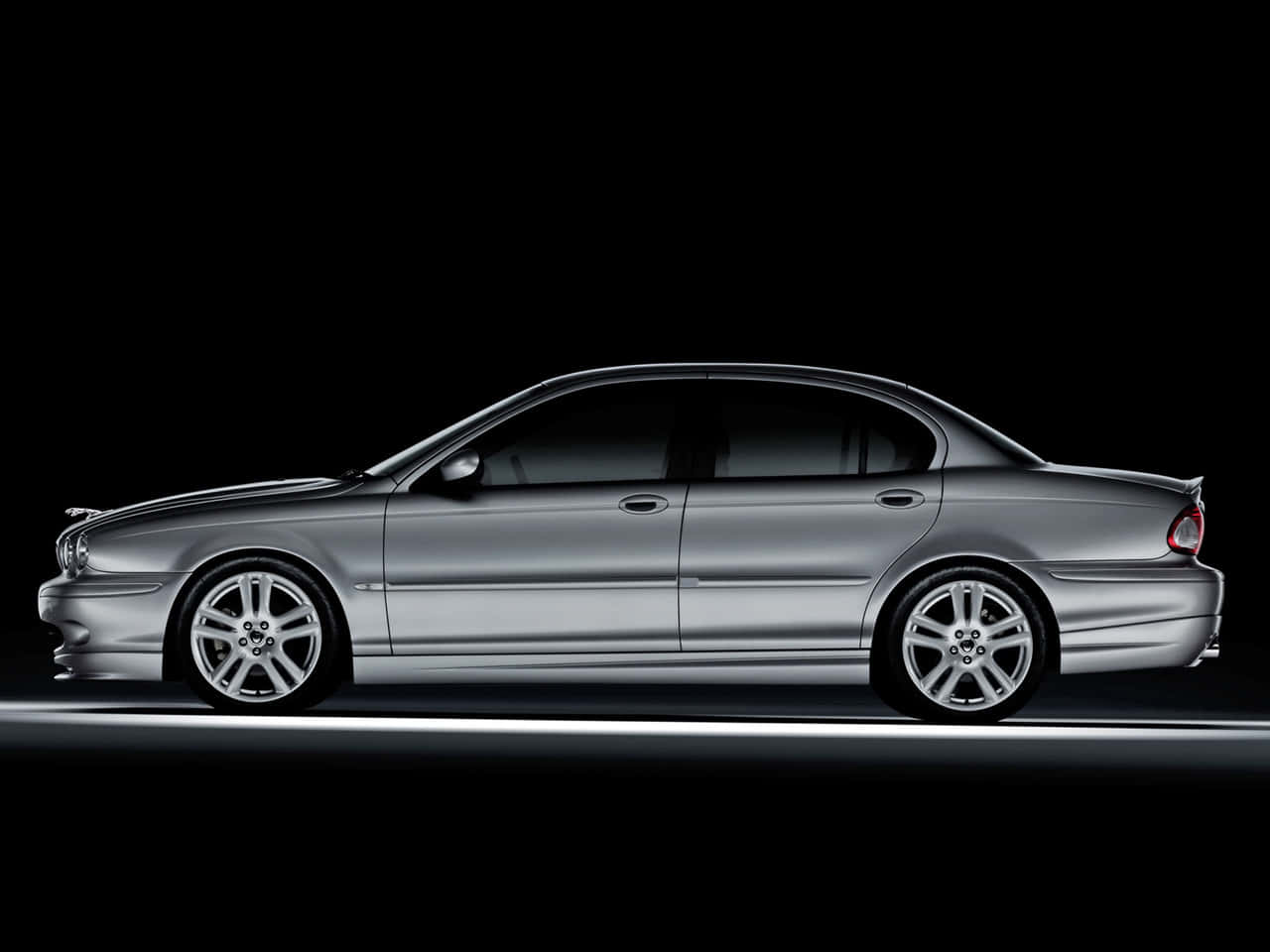 Jaguar X-type 桌布 壁紙 — 一輛時尚的銀色轎車在黑色背景上側面滑行，帶有發光的底盤燈條。