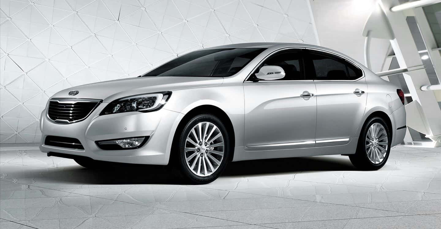 Kia Cadenza 桌布 壁紙 — 一輛時尚的銀色轎車在工作室燈光下閃耀，背景是現代白色幾何圖案。