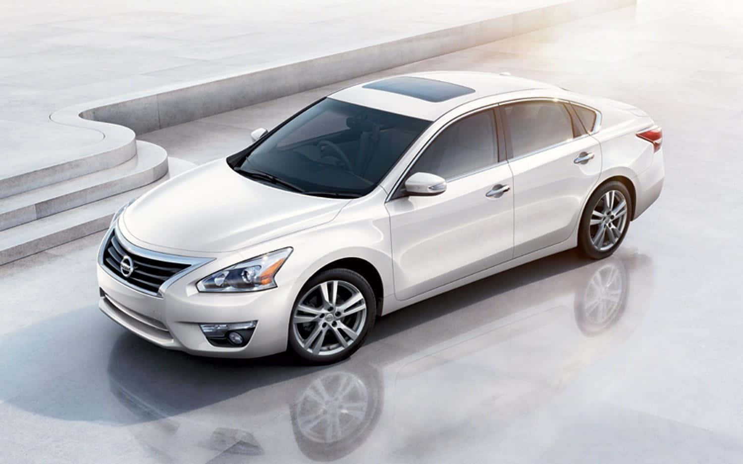 Nissan Altima 桌布 壁紙 — 一輛時尚的銀色轎車在柔和日光下，在帶有弧形階梯的簡約混凝土平台上閃閃發光。