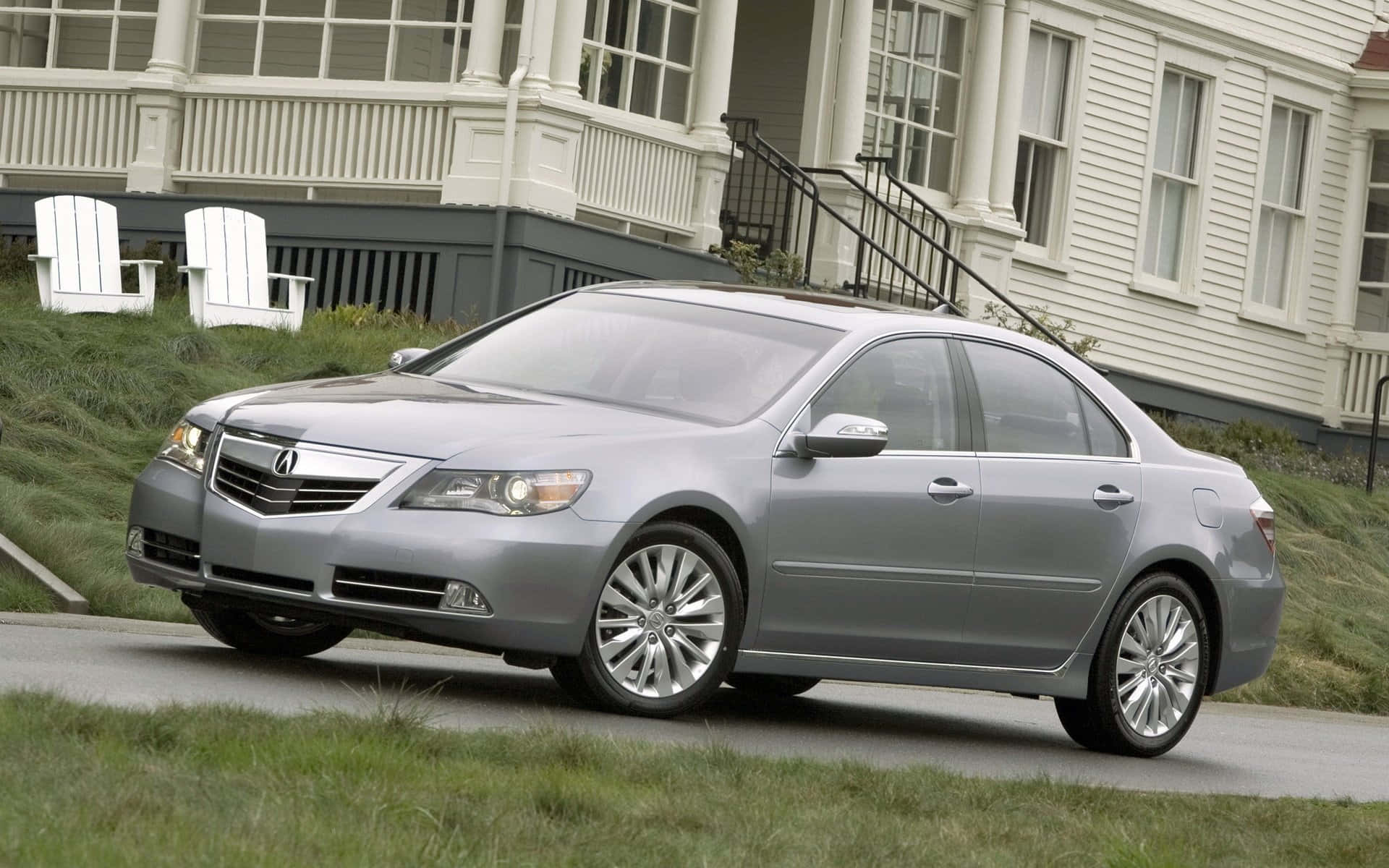 Acura Rl 桌布 壁紙 — 一輛時尚的銀色轎車停放在白色房屋前的鋪砌道路上，房屋前有草坪椅和綠草。