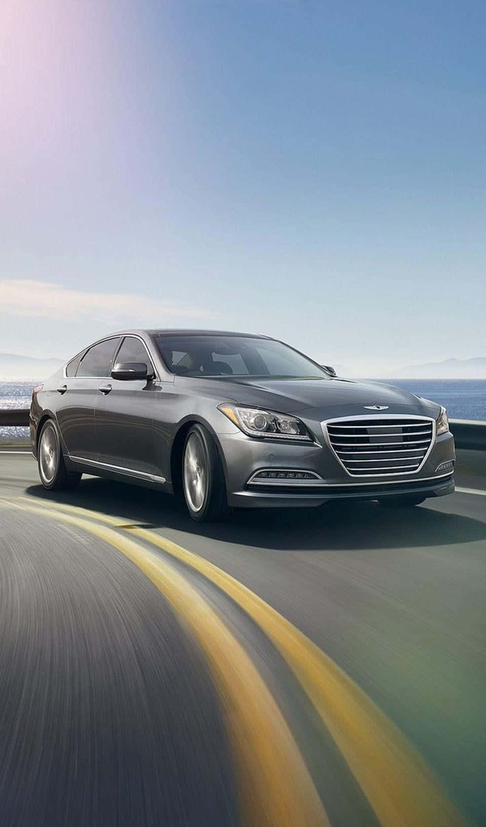 Genesis G80 桌布 壁紙 — 一輛時尚的銀色轎車沿著海岸高速公路疾馳，在晴朗的藍天下留下模糊的運動線條。