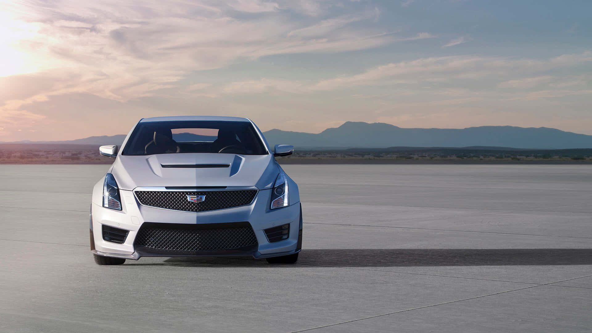 Cadillac Ats 桌布 壁紙 — 一架流線型銀色跑車在廣闊的沙漠跑道上，於黃金時刻蓄勢待發，遠山在柔和粉彩天空下若隱若現。