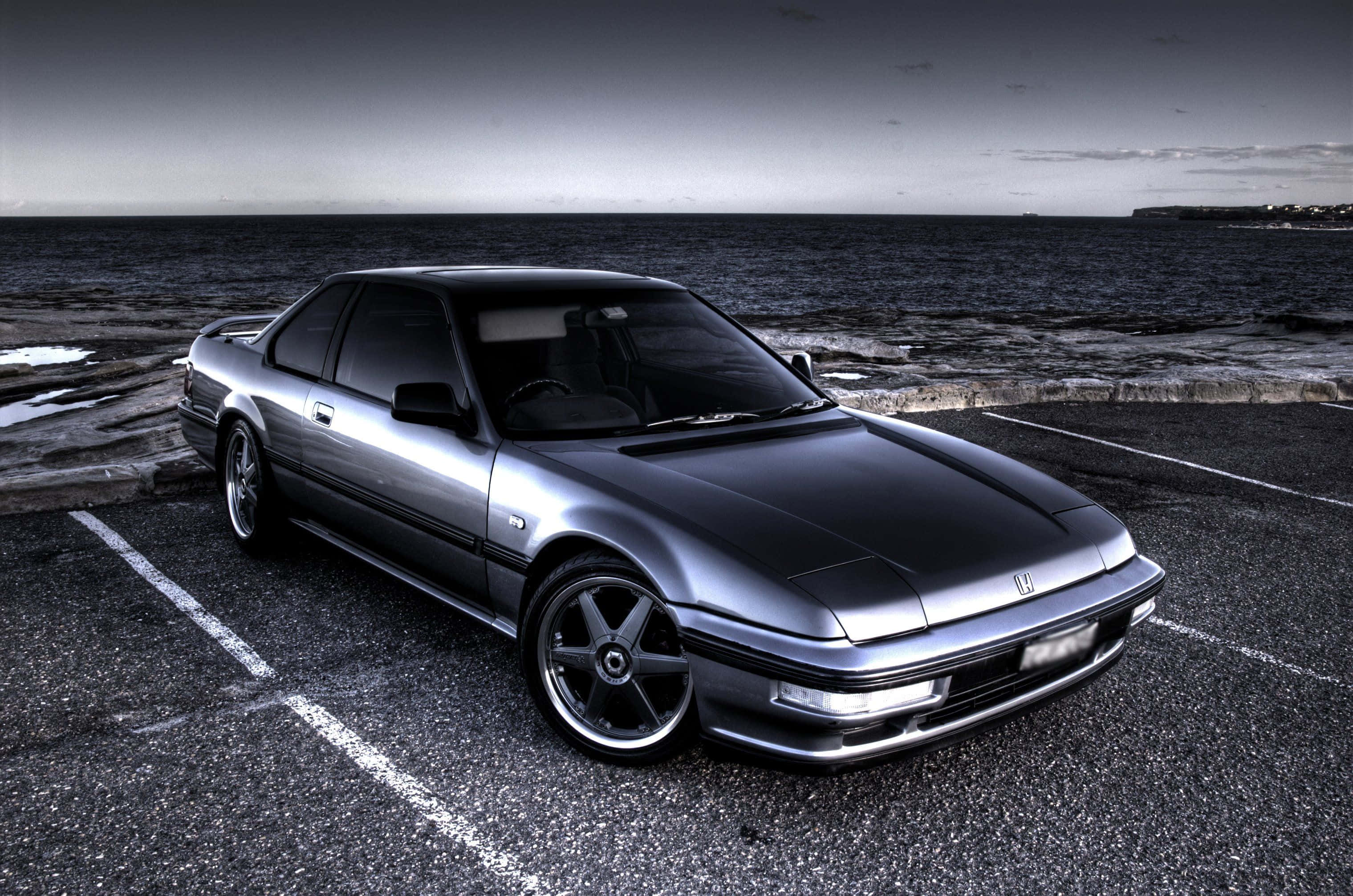 Honda Prelude 桌布 壁紙 — 一輛時尚的銀色跑車停放在沿海的瀝青停車場，背景是海洋和天空。