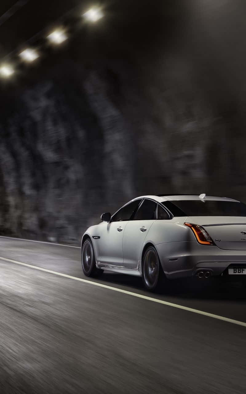 Jaguar Xjr 桌布 壁紙 — 一輛時尚的銀色跑車在燈光昏暗的隧道中疾馳，道路上有動態模糊，頭頂燈光投下戲劇性的陰影。