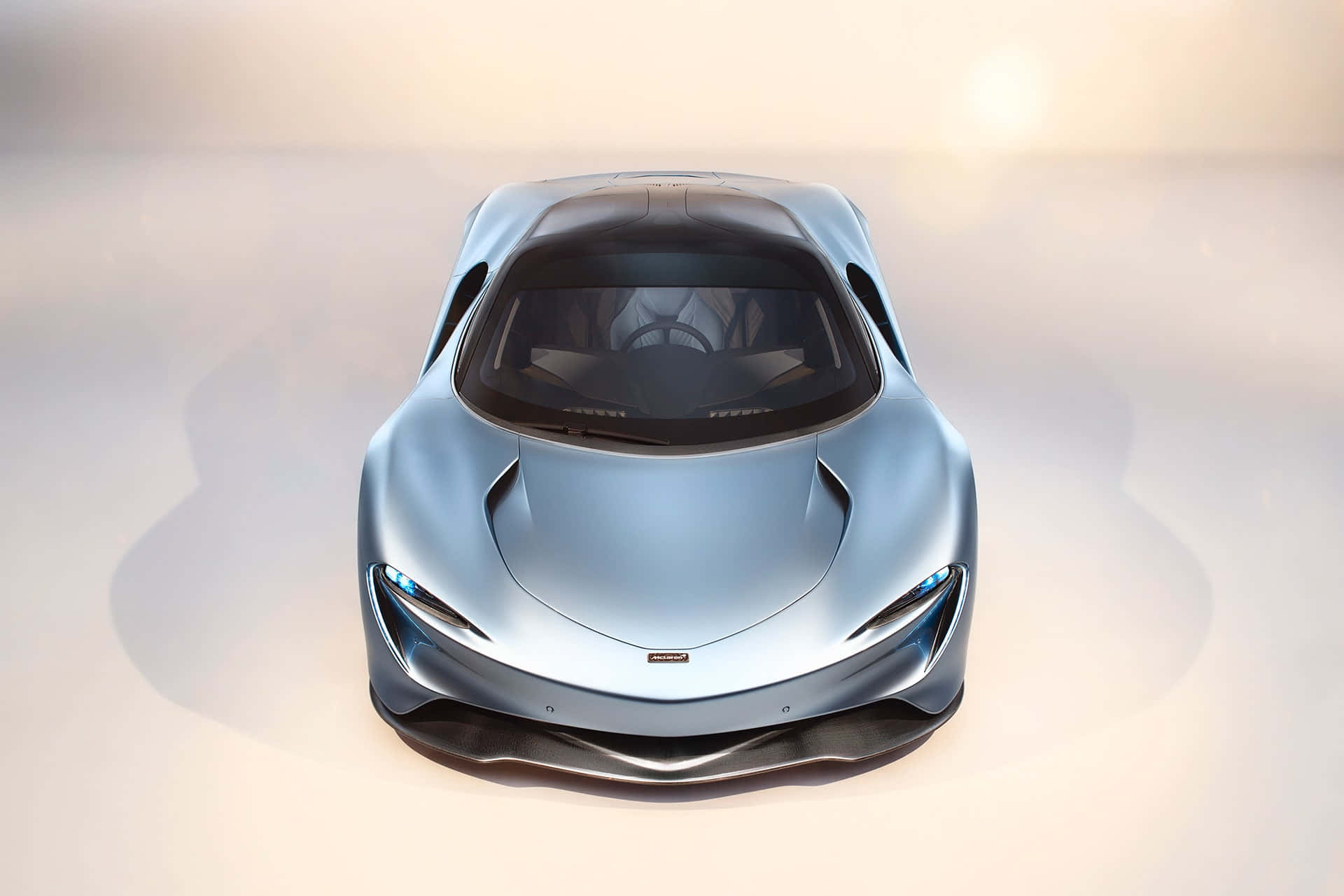 Mclaren Speedtail 桌布 壁紙 — 從上方俯瞰，一輛時尚的銀色跑車配備發光的藍色車頭燈，背景為柔和的白色。