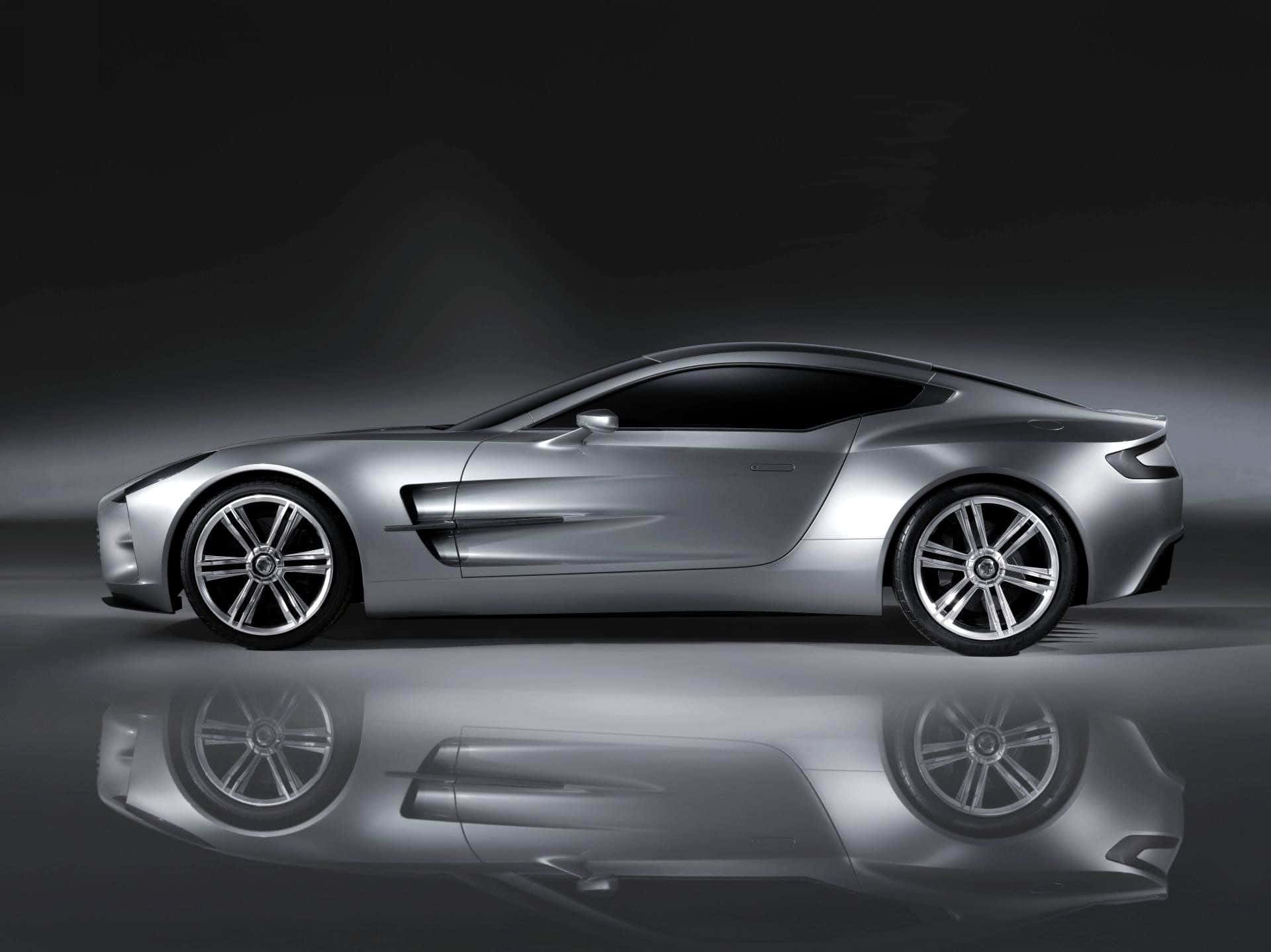 Aston Martin One-77 桌布 壁紙 — 一輛線條流暢的銀色跑車，表面反光，在設有鏡面地板的暗色工作室背景中展示。
