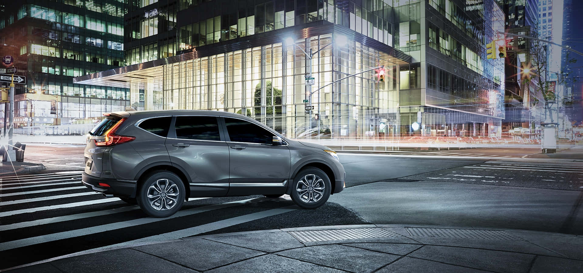 Honda Cr-v 桌布 壁紙 — 一輛時尚的銀色SUV在夜間停泊於城市行人穿越道，周圍是閃爍的霓虹燈和高聳的玻璃建築。