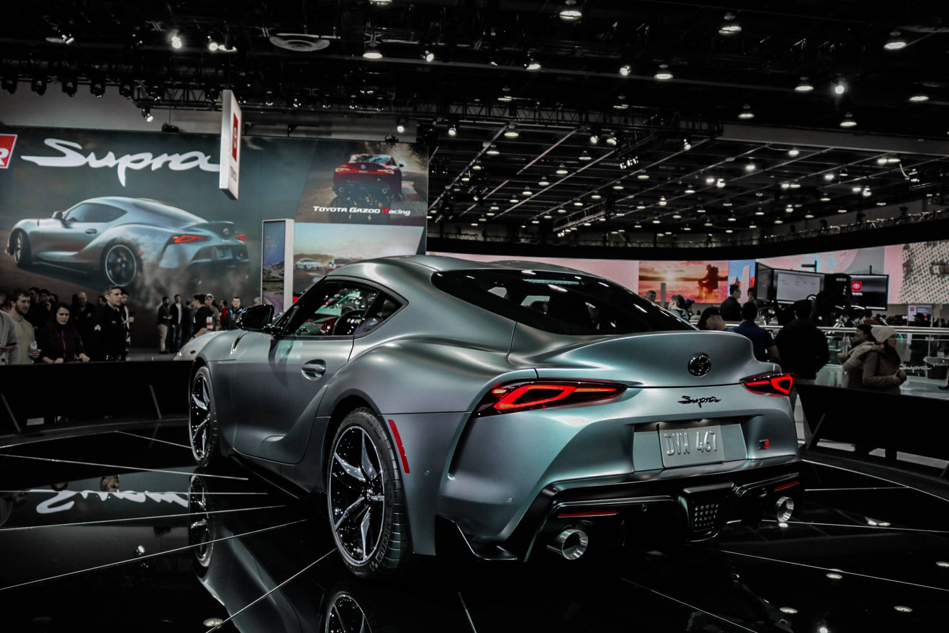 銀色豐田Supra跑車在車展上展出，周圍有人群和明亮的燈光。 — Toyota Supra 壁紙