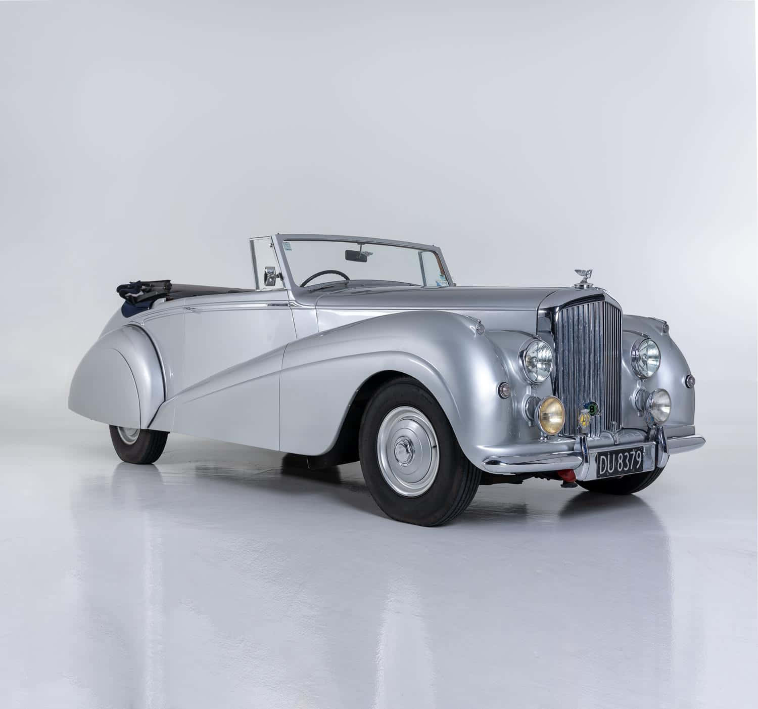 Bentley Mark Vi 桌布 壁紙 — 一輛時尚的銀色復古敞篷跑車，帶有鍍鉻裝飾和軟頂，擺放在反射性白色工作室地板上。