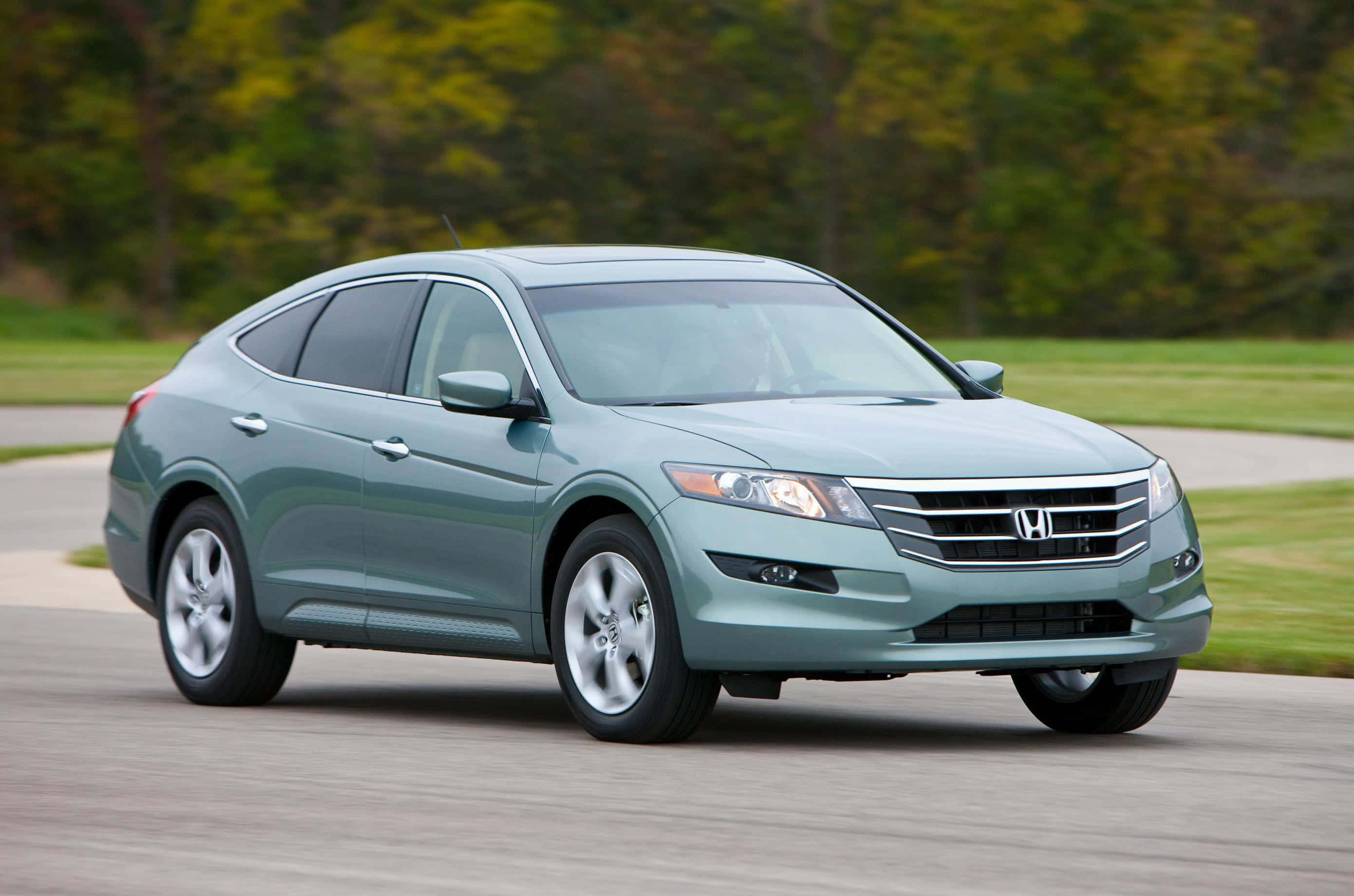 Honda Crosstour 桌布 壁紙 — 一輛時尚的青色本田 Crosstour SUV 在鋪砌的道路上平穩行駛，背景是模糊的綠色樹木和草地。