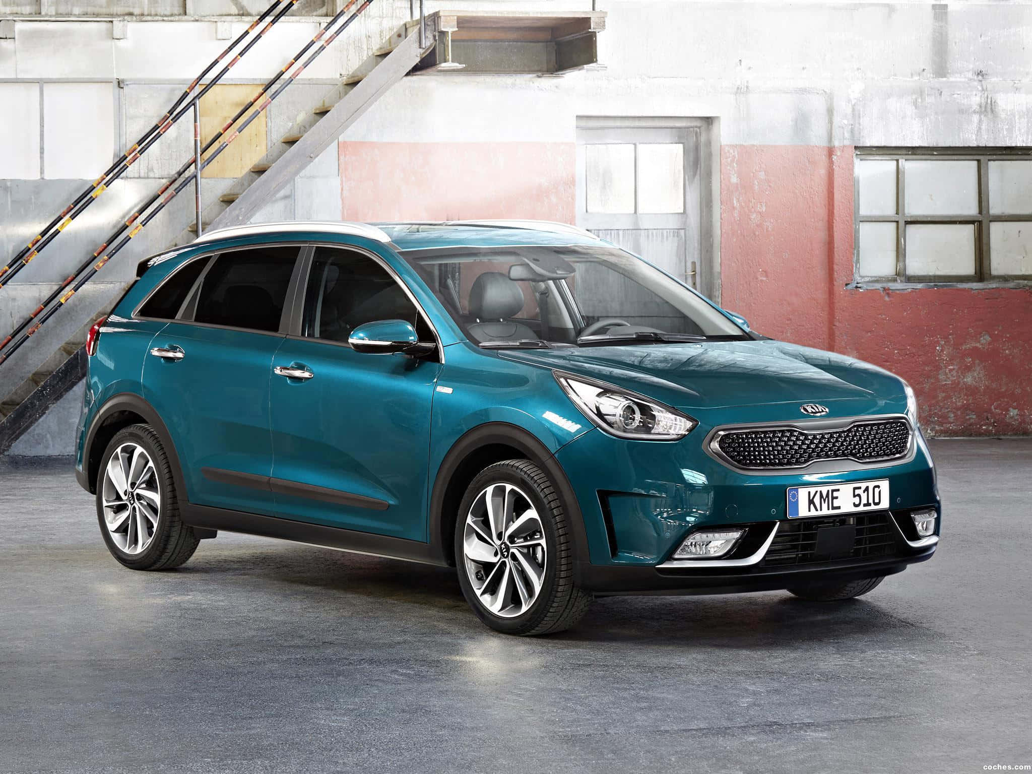 Kia Niro 桌布 壁紙 — 一架時尚的青綠色Kia Niro SUV停放在風化的工業倉庫內，帶有外露樓梯和褪色牆壁。