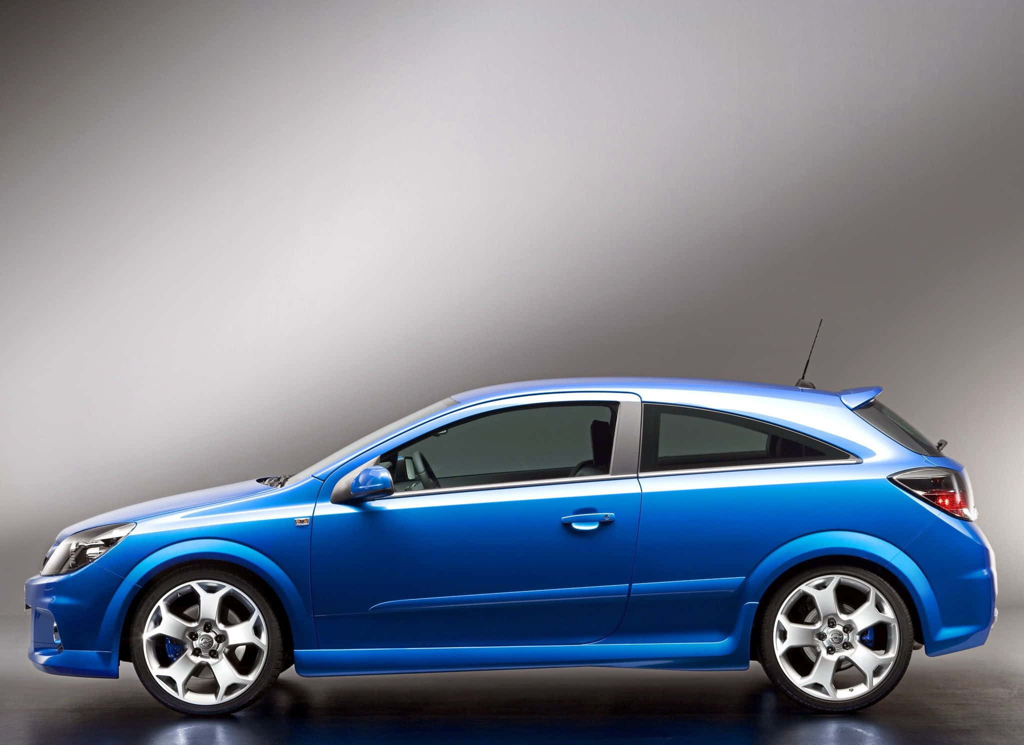 Opel Astra 桌布 壁紙 — 一輛時尚亮麗的藍色跑車，在漸變灰色工作室背景前以側面展示。
