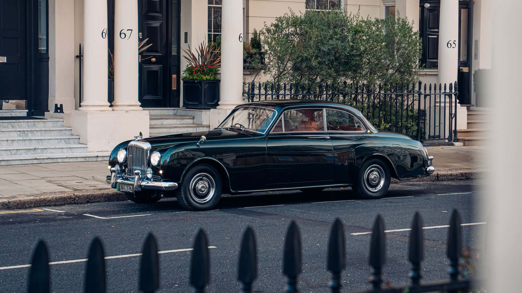 Bentley S2 桌布 壁紙 — 一台時尚的復古綠色賓利轎車停放在寧靜的住宅街道上，街道兩旁是優雅的聯排別墅和黑色鍛鐵圍欄。
