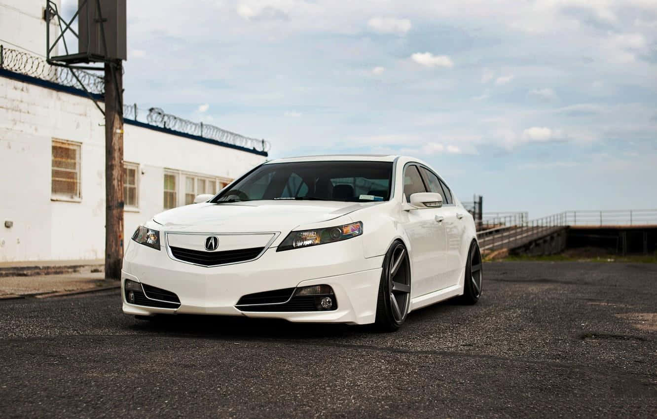 Acura Tsx 桌布 壁紙 — 一輛時尚的白色Acura TL運動轎車，配備定制輪圈，停在有刺鐵絲網的白色建築附近的瀝青路上。