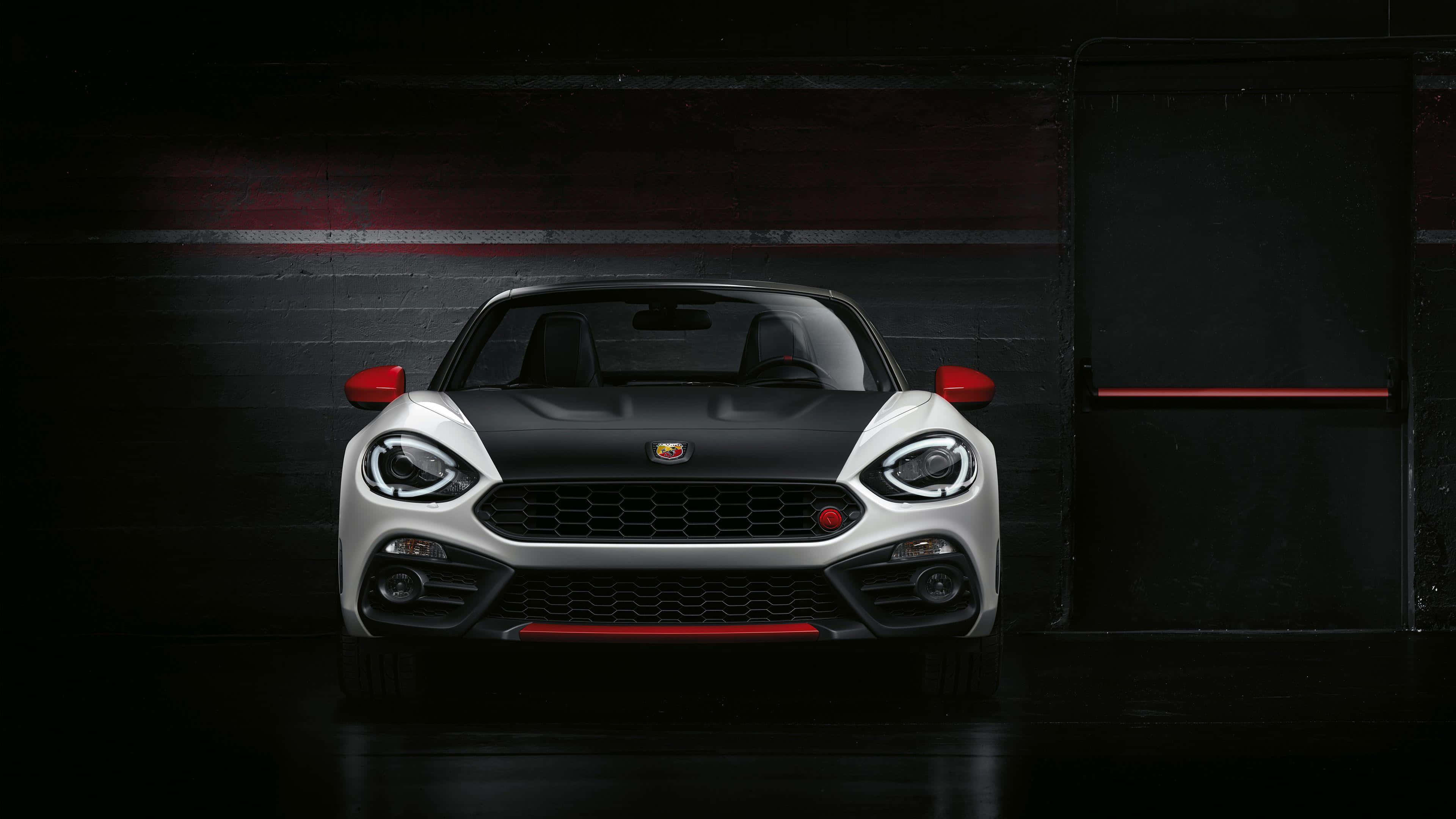 Abarth 桌布 壁紙 — 一輛時尚的白色和黑色跑車帶有紅色點綴，在帶有紅色高光的黑暗車庫中被戲劇性地照亮。