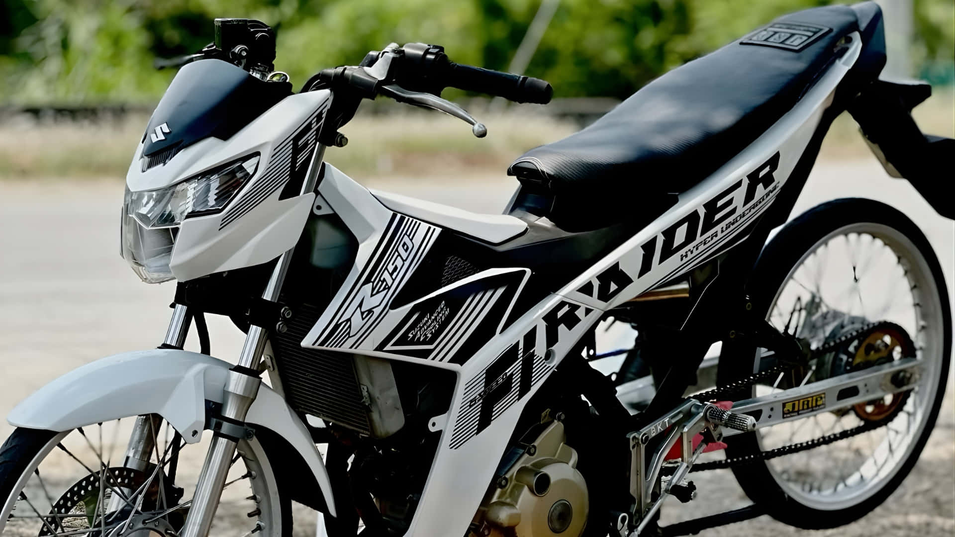  壁紙 — 一台時尚的黑白 Suzuki 機車，帶有醒目圖案，停放在鋪砌路面上，背景有綠植。