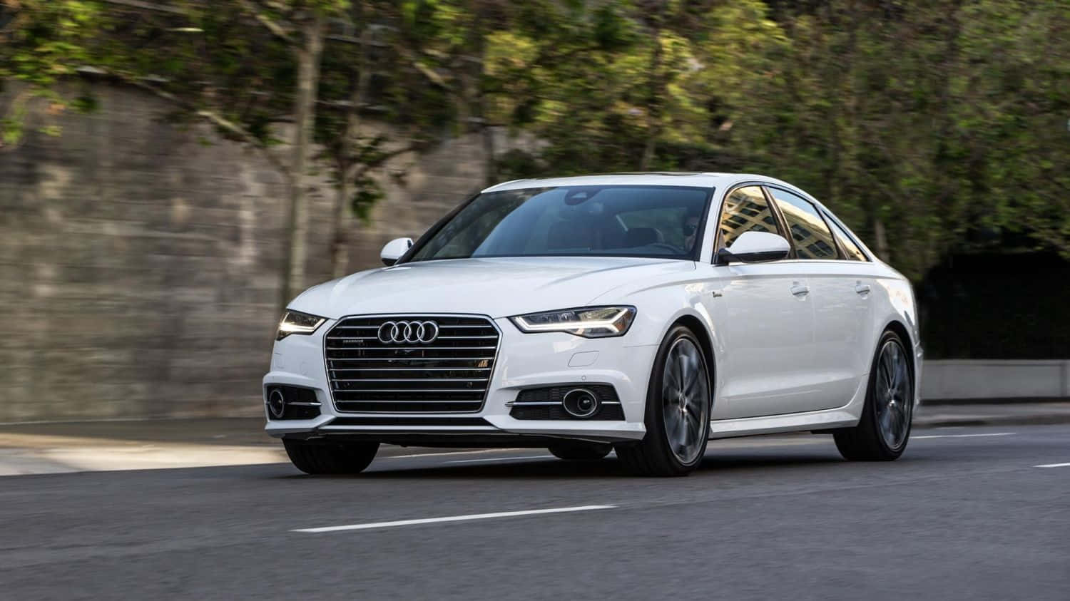 Audi S6 桌布 壁紙 — 一輛時尚的白色奧迪轎車沿著綠樹成蔭的道路平穩行駛，背景帶有動態模糊效果。