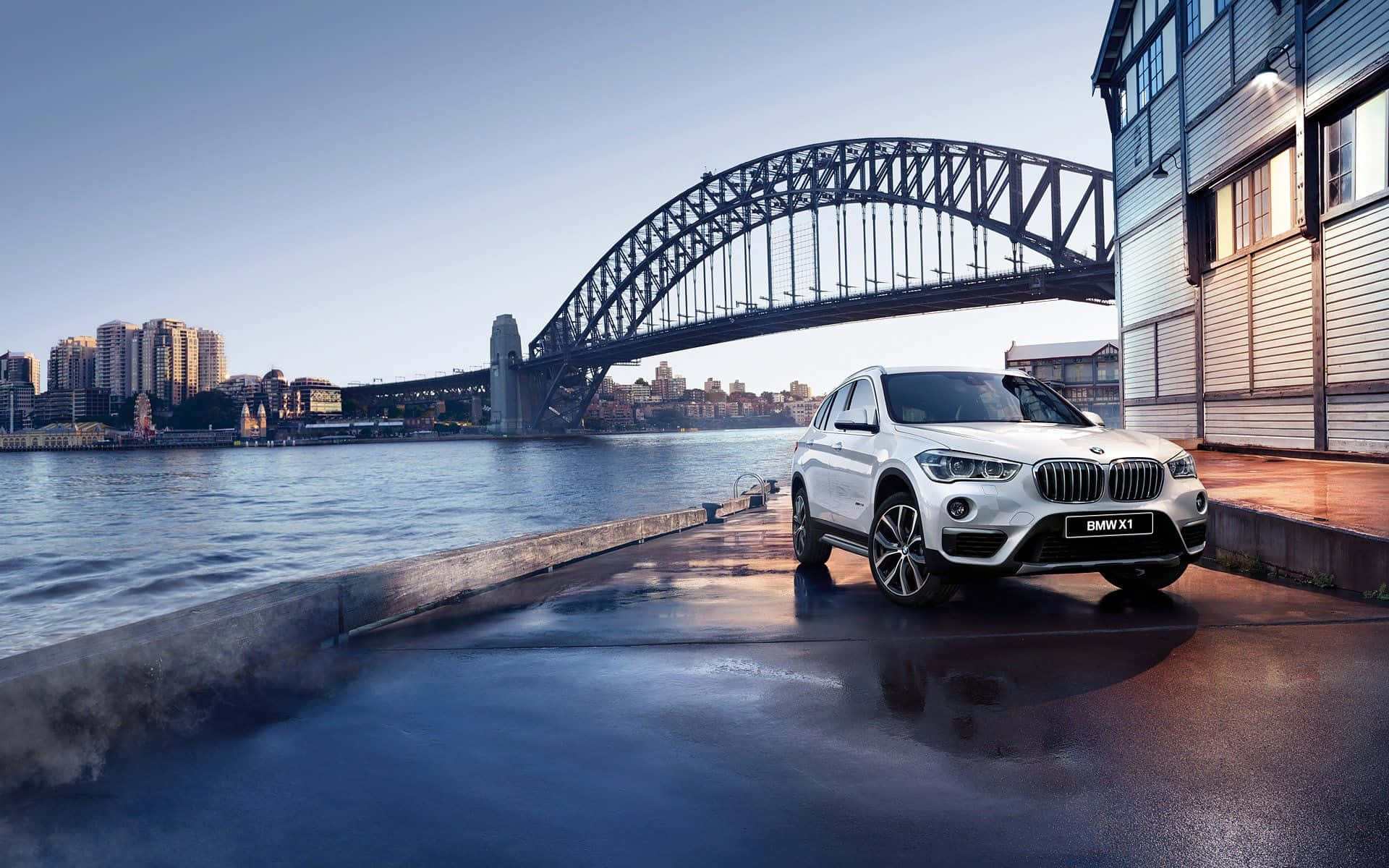 Bmw I8 桌布 壁紙 — 一輛時尚的白色BMW X1 SUV停泊在濕漉漉的碼頭上，背景是標誌性的雪梨港灣大橋，天空清澈湛藍。