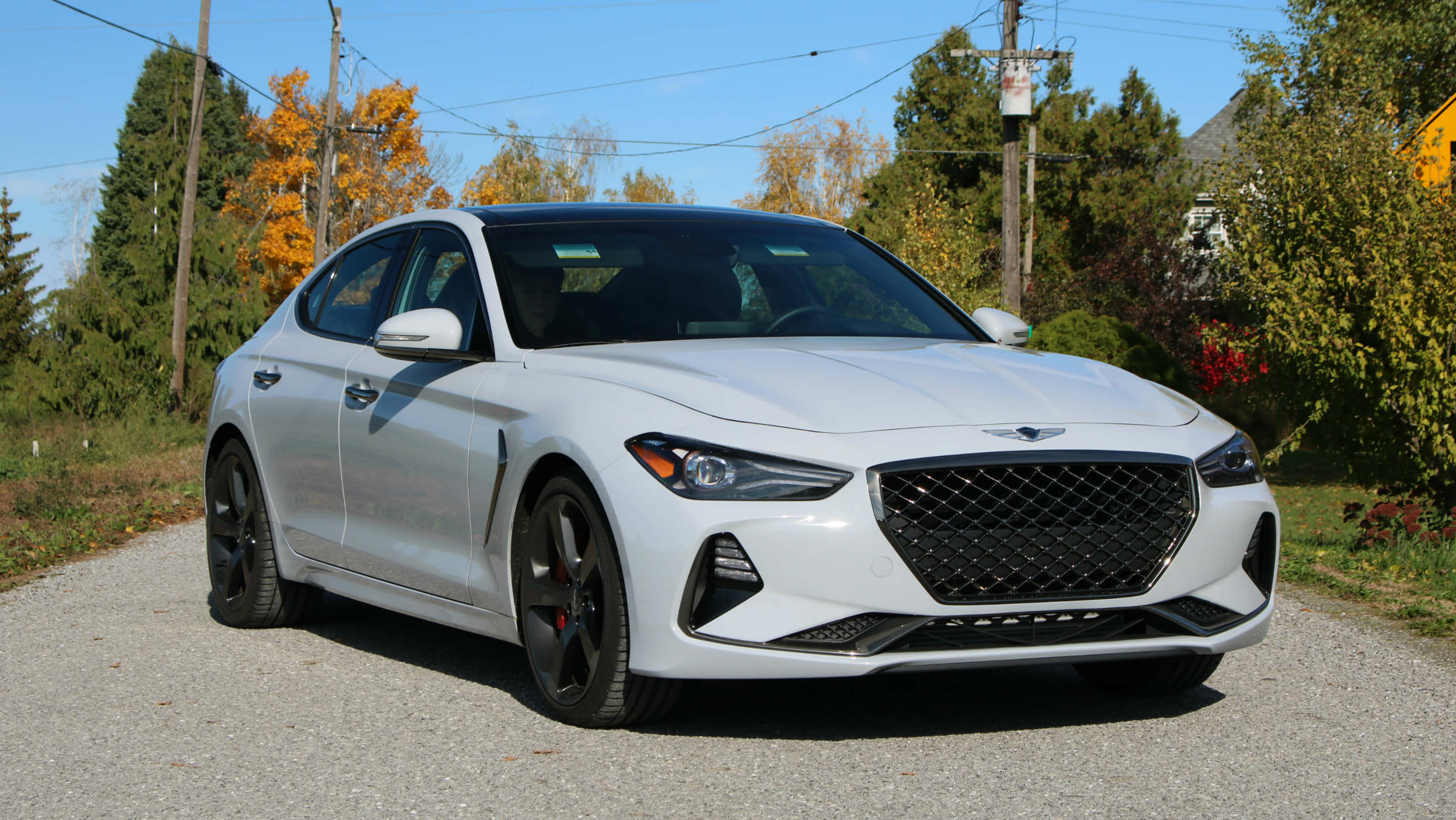 Genesis G70 桌布 壁紙 — 一輛時尚的白色Genesis G70運動轎車停在碎石路上，周圍是秋天的樹木，天空清澈湛藍。
