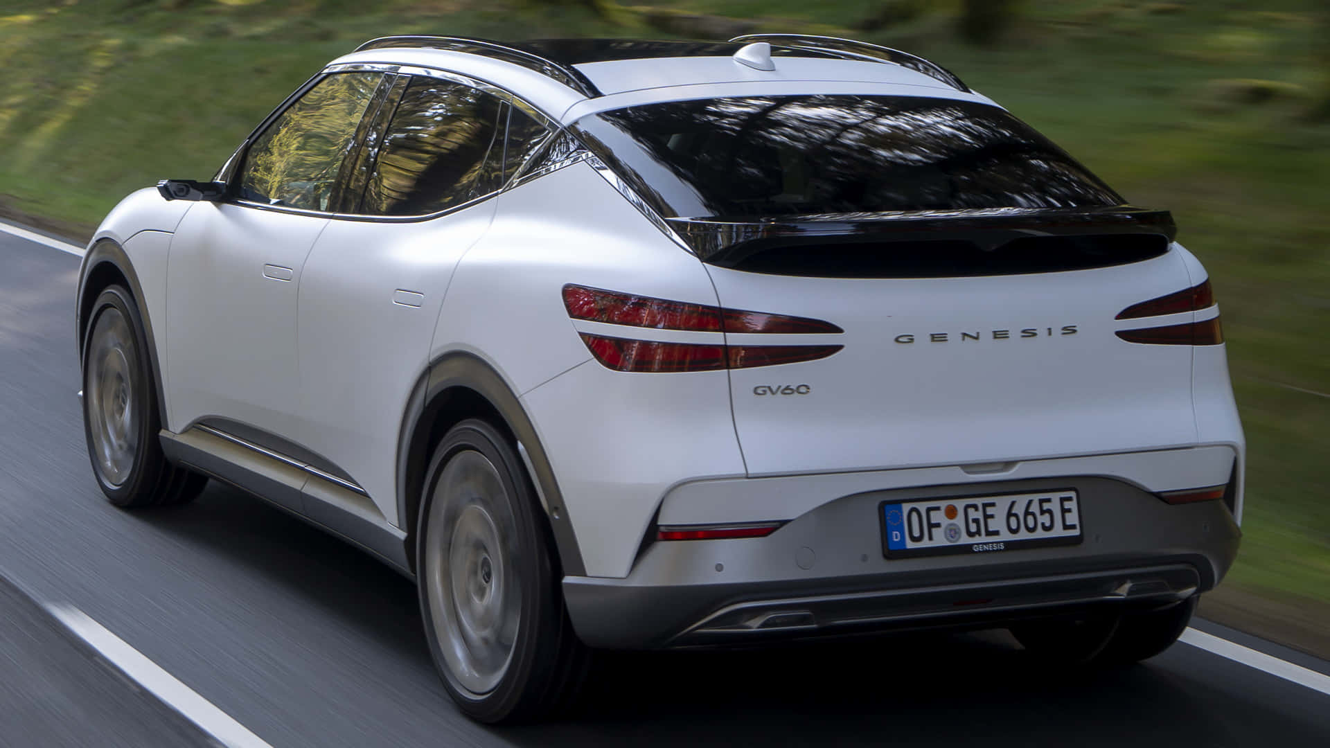 Genesis Gv60 桌布 壁紙 — 一輛時尚的白色 Genesis GV60 電動 SUV 在陽光明媚的道路上行駛，模糊的綠意飛馳而過。