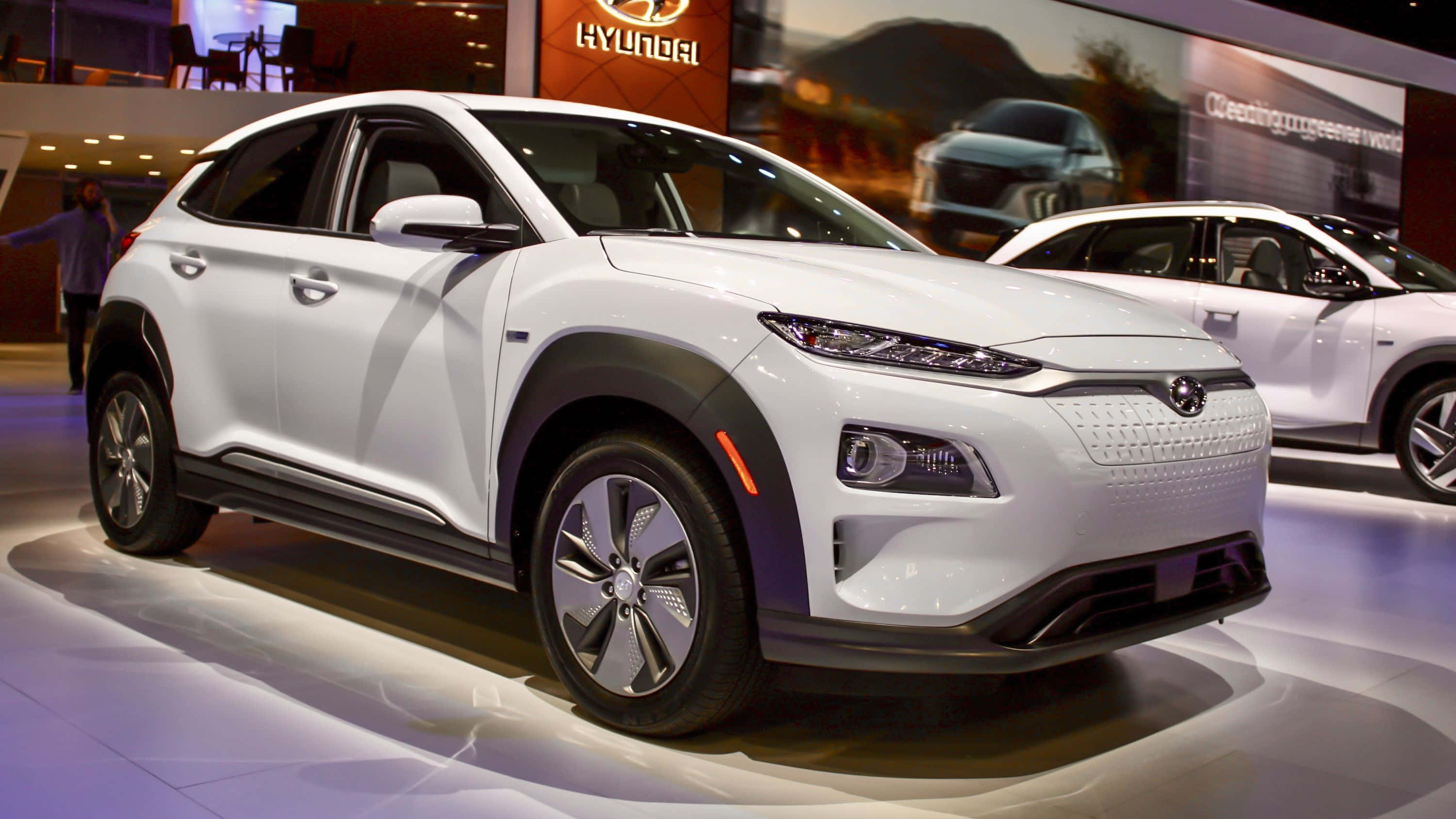 Hyundai Kona 桌布 壁紙 — 一輛時尚的白色現代Kona電動SUV在明亮的展廳燈光下閃耀，地面反射出光澤。