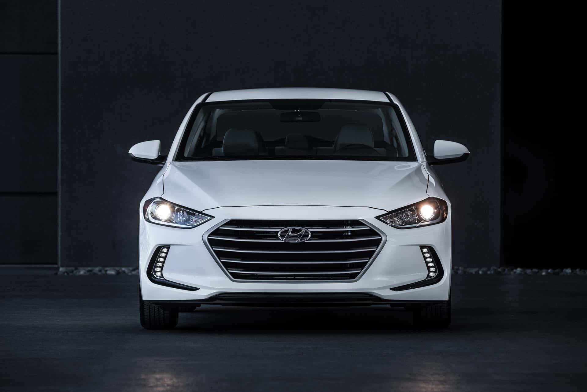 Hyundai Elantra 桌布 壁紙 — 一輛時尚的白色現代轎車正面朝前，配備發光頭燈，背景為深色簡約工作室。