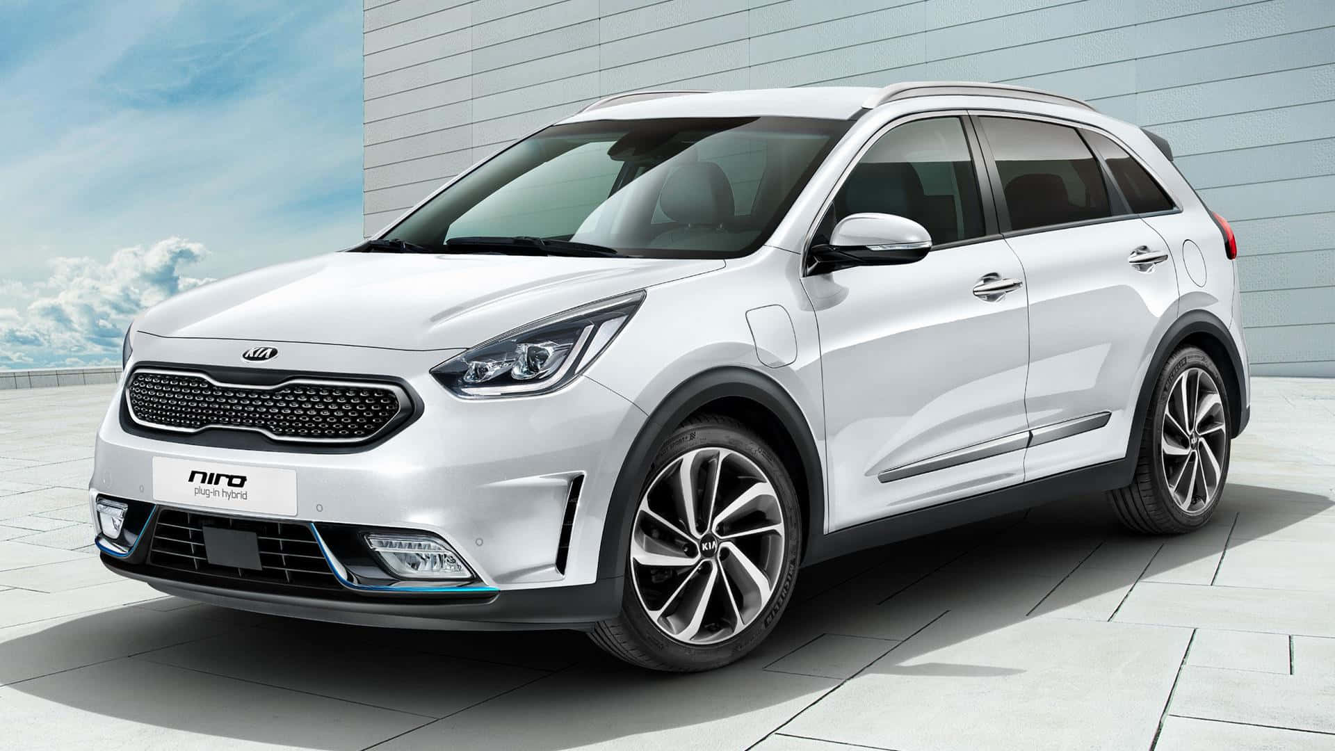 Kia Niro 桌布 壁紙 — 一輛時尚的白色Kia Niro插電式混合動力SUV停放在瓷磚屋頂上，背景為現代建築和藍天白雲。