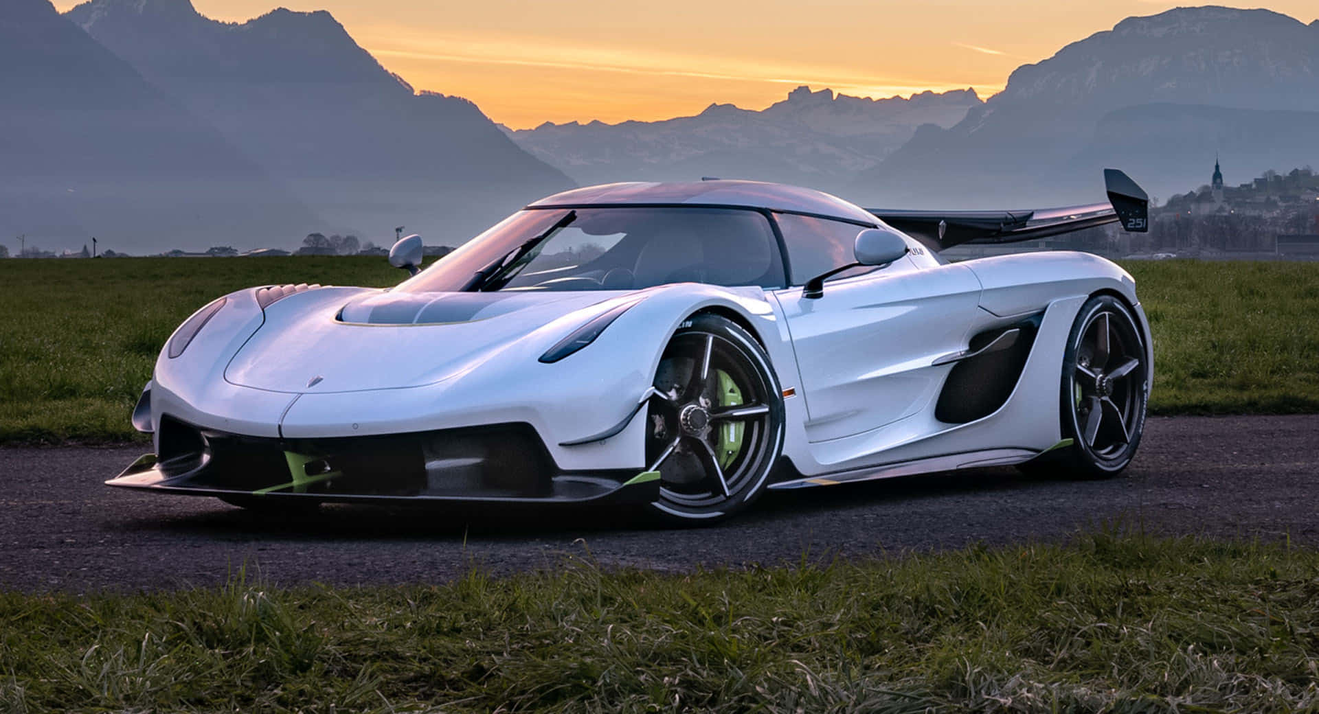  壁紙 — 一台時尚的白色 Koenigsegg 超級跑車，帶有萊姆綠色點綴，在日落時分停泊在碎石路上，背景是山區地形。