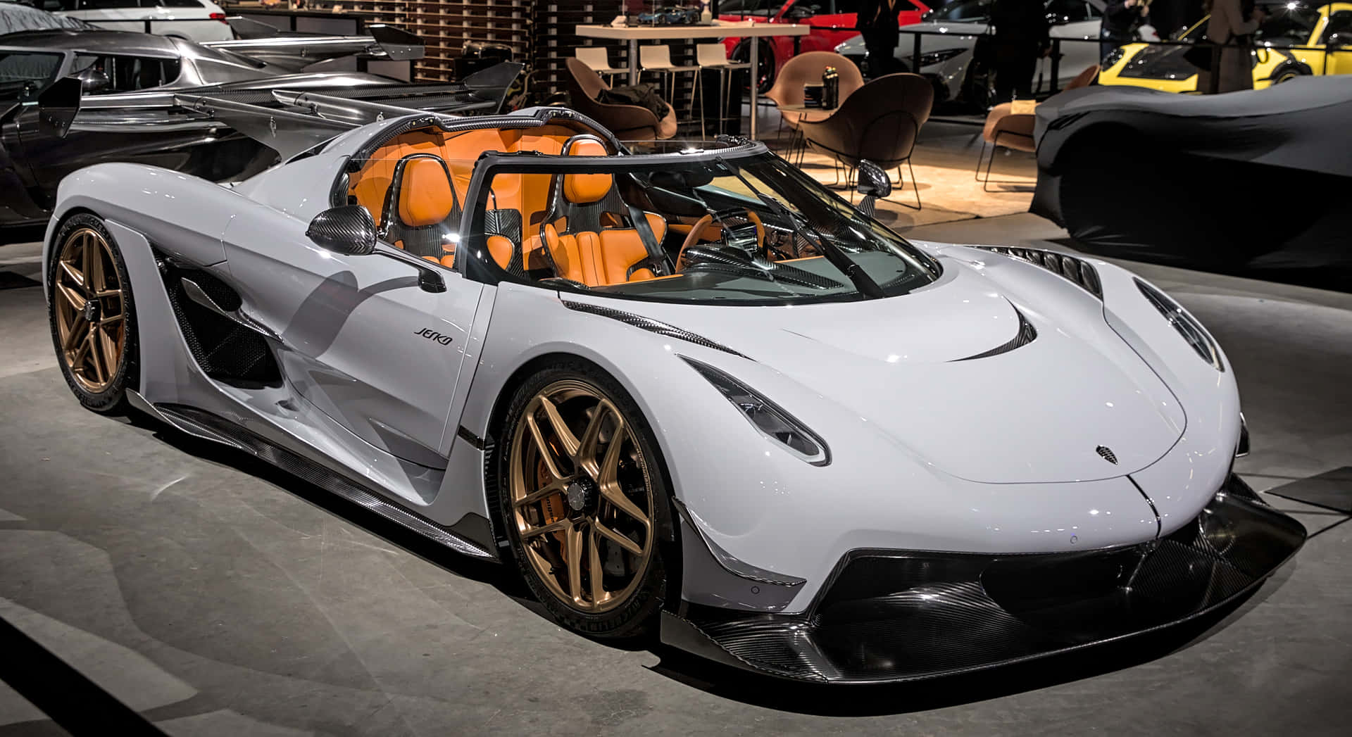  壁紙 — 一輛時尚的白色Koenigsegg Jesko，配備橙色內裝和金色輪圈，在車展的明亮燈光下閃閃發光。