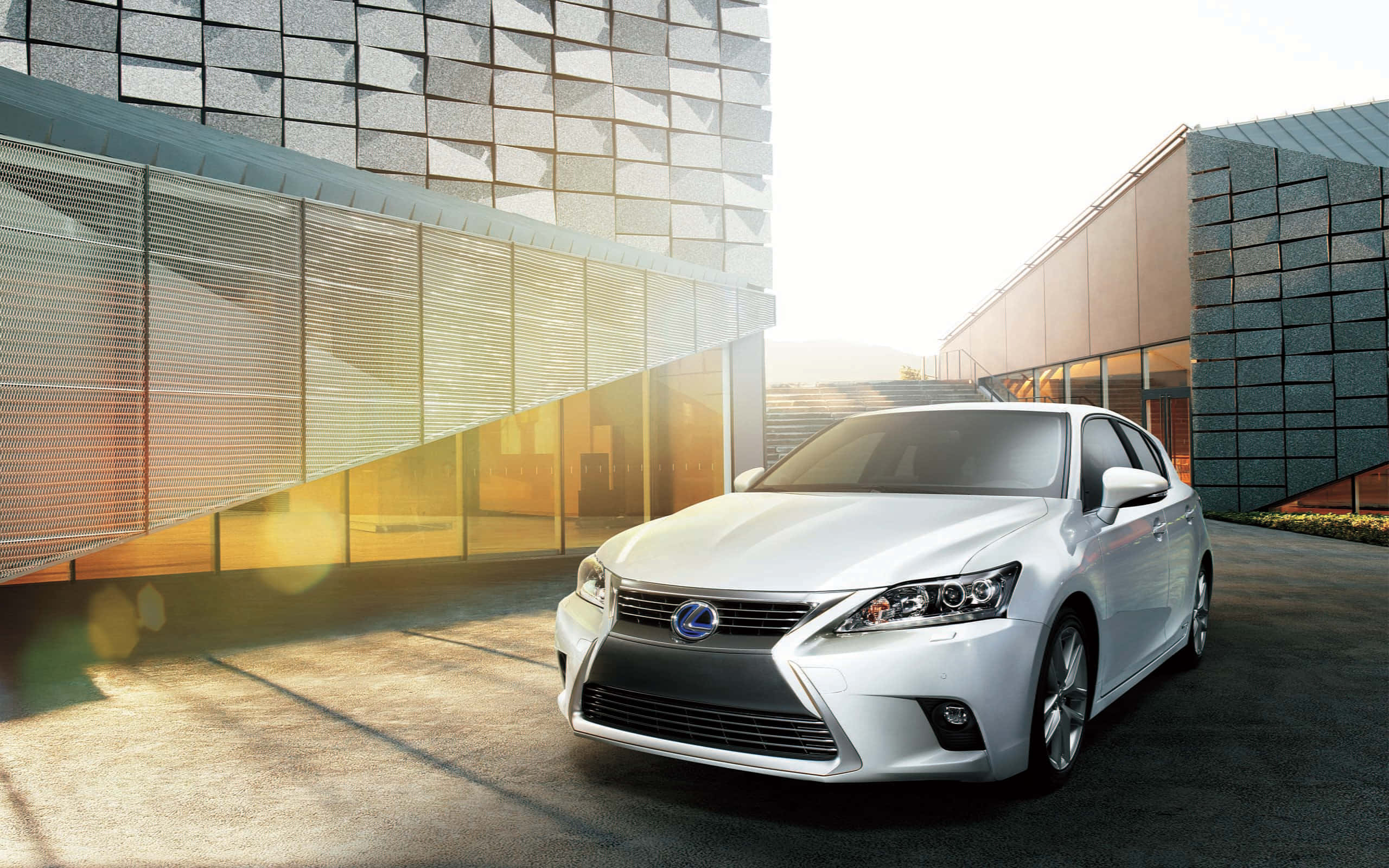 Lexus Ct 200h 桌布 壁紙 — 一輛時尚的白色Lexus轎車在金色陽光下閃耀，位於現代幾何建築之間，建築物帶有反光玻璃外牆。