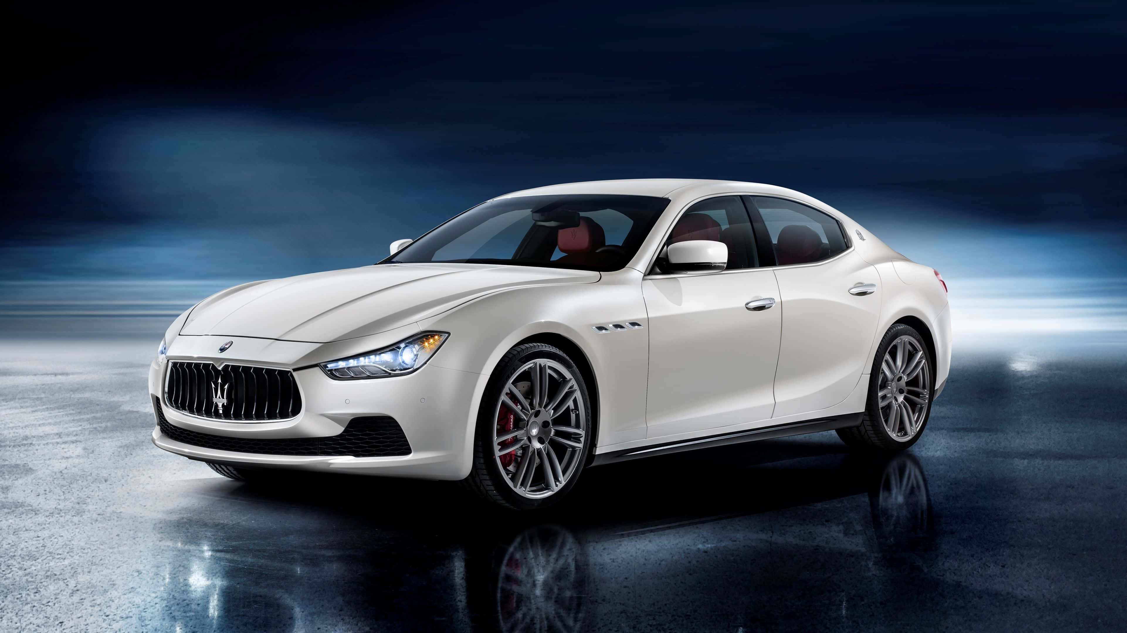 Maserati Ghibli 桌布 壁紙 — 一輛時尚的白色瑪莎拉蒂跑車在戲劇性的藍色燈光下，在反光的濕滑表面上閃閃發光。