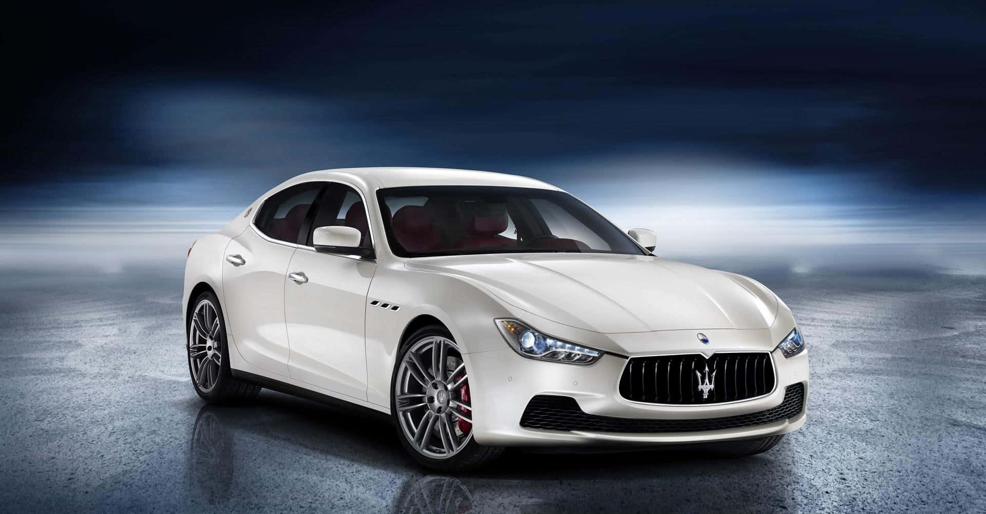 Maserati Ghibli 桌布 壁紙 — 一輛時尚的白色瑪莎拉蒂跑車在戲劇性的攝影棚燈光下，在憂鬱的藍灰色背景上閃閃發光。