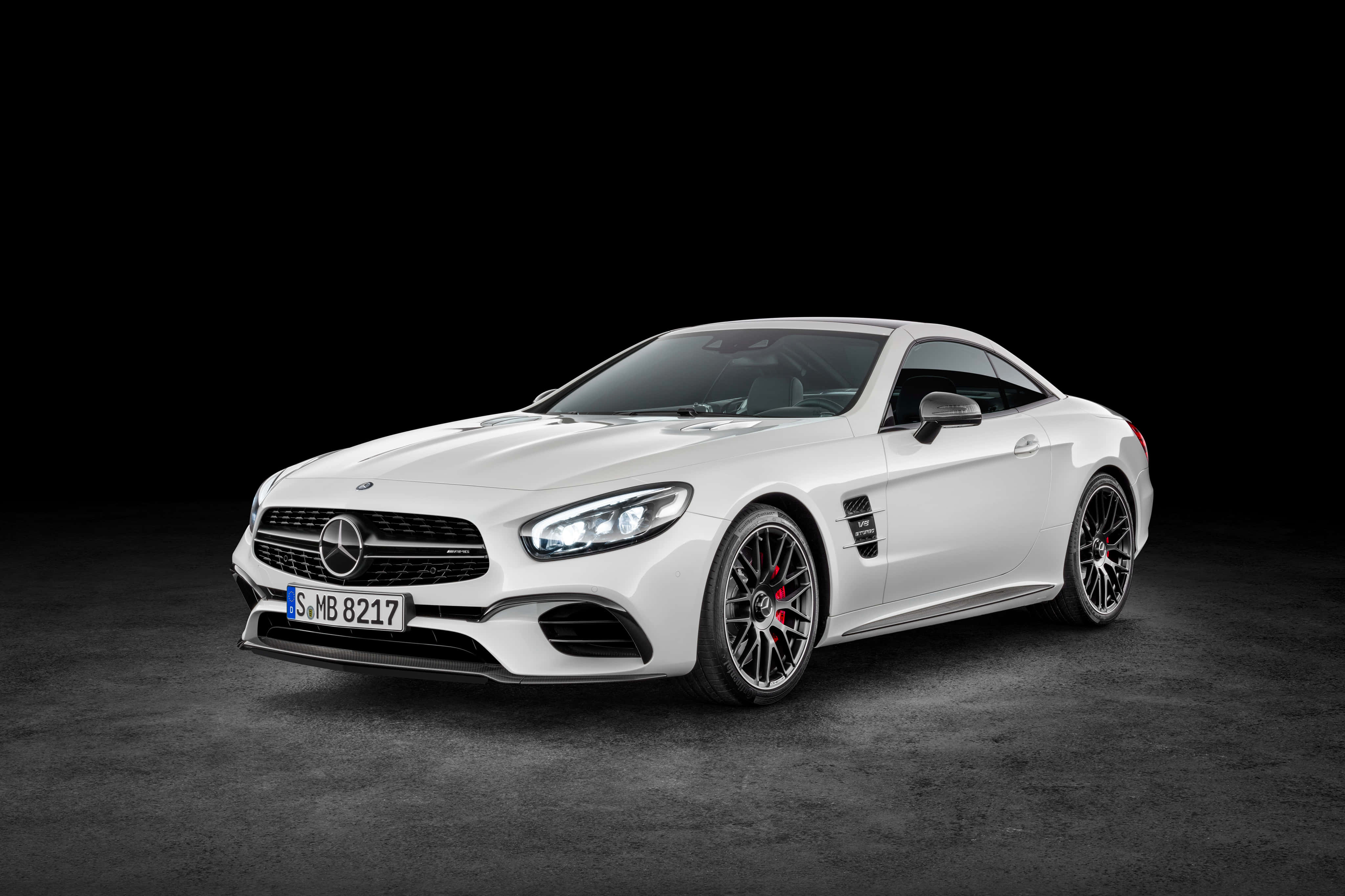 Mercedes Benz Sl-class 桌布 壁紙 — 一輛流線型白色 Mercedes-AMG SL63 跑車，配備黑色輪圈和紅色制動卡鉗，在黑色背景的暗色工作室地板上蓄勢待發。
