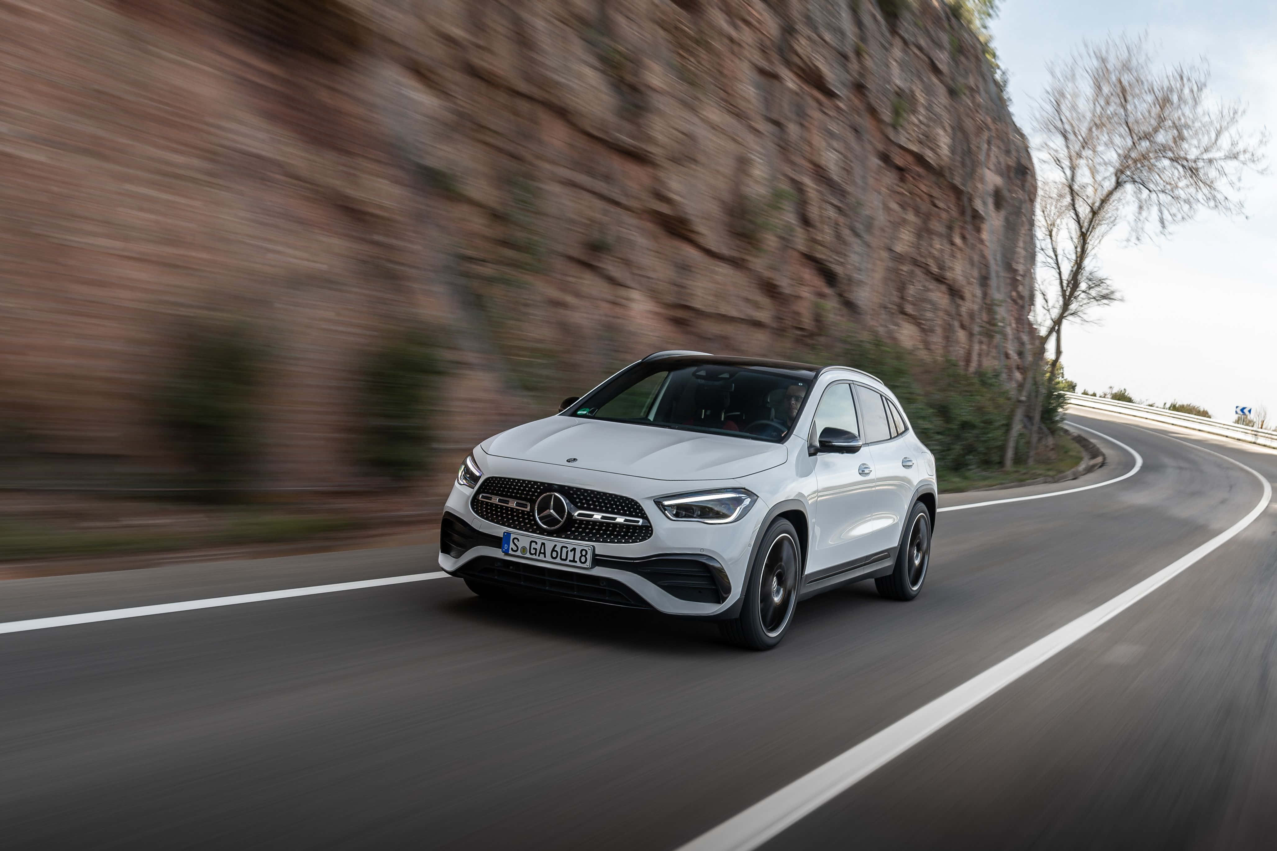 Mercedes Benz Gla-class 桌布 壁紙 — 一架時尚的白色 Mercedes-Benz GLA 45 AMG 沿著蜿蜒的山路疾馳，背景是模糊的岩石峭壁。
