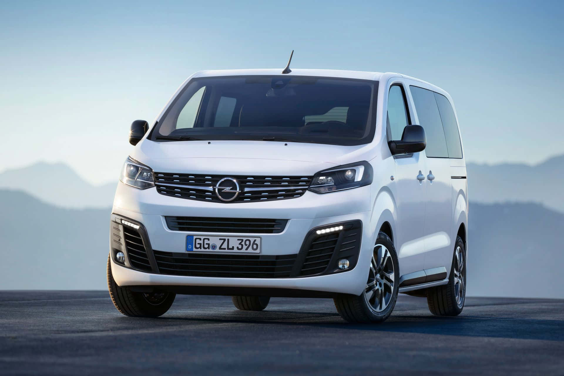 Opel Zafira 桌布 壁紙 — 一輛時尚的白色Opel Zafira Tourer客貨車停泊在鋪砌道路上，背景是朦朧的山脈，天空清澈湛藍。