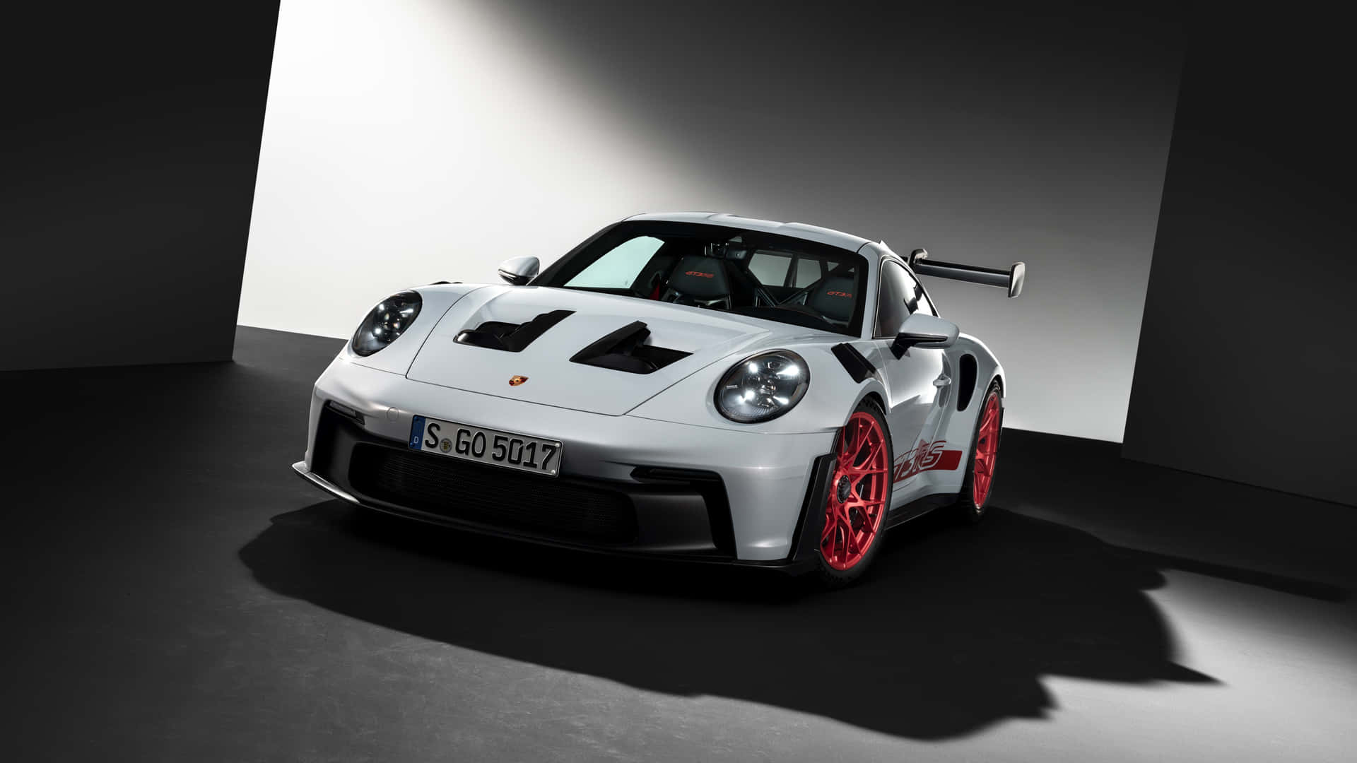  壁紙 — 一輛時尚的白色保時捷 911 GT2 RS，配備紅色輪圈和黑色飾件，在極簡主義的攝影棚環境中戲劇性地被照亮。