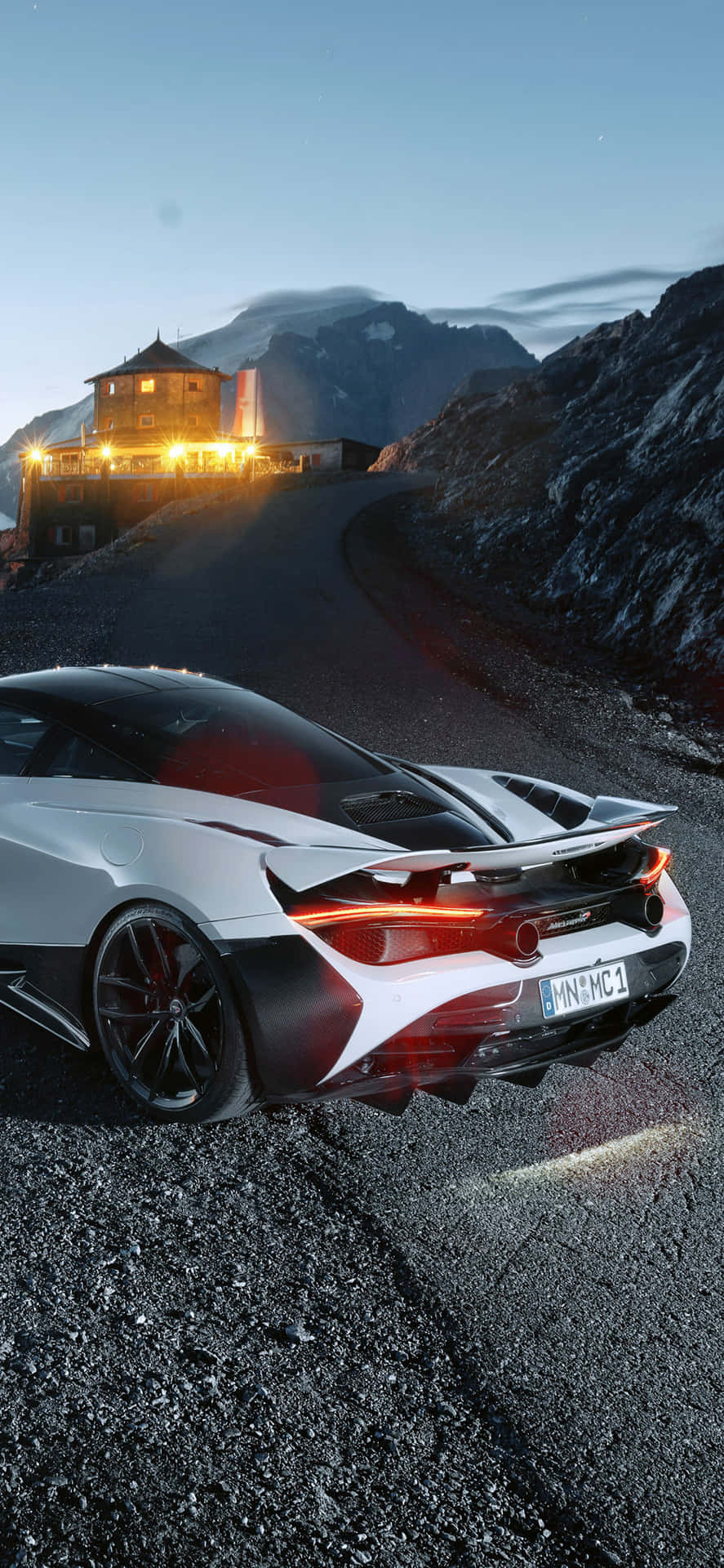 白色跑車停泊在黃昏時分的山路上，附近有照明建築物。 — Project Cars 2 壁紙