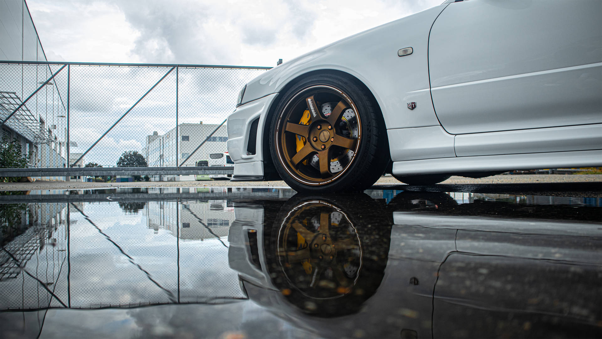 陰天時，白色跑車配金色輪圈在水坑中的倒影。 — 日產 Skyline GTR R34 壁紙