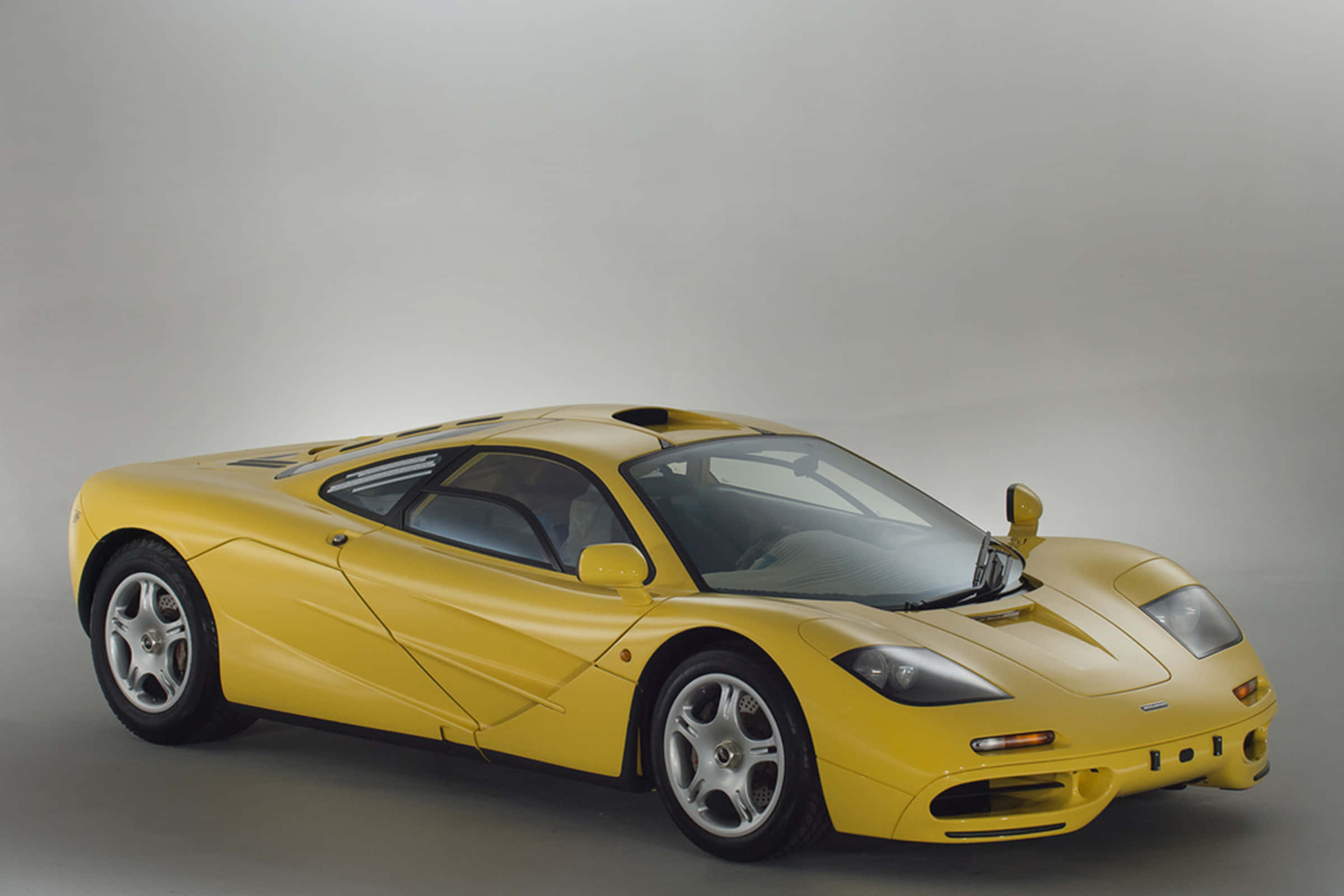 Mclaren F1 桌布 壁紙 — 一輛時尚的黃色McLaren F1超級跑車以四分之三角度擺放在中性灰色工作室背景前。