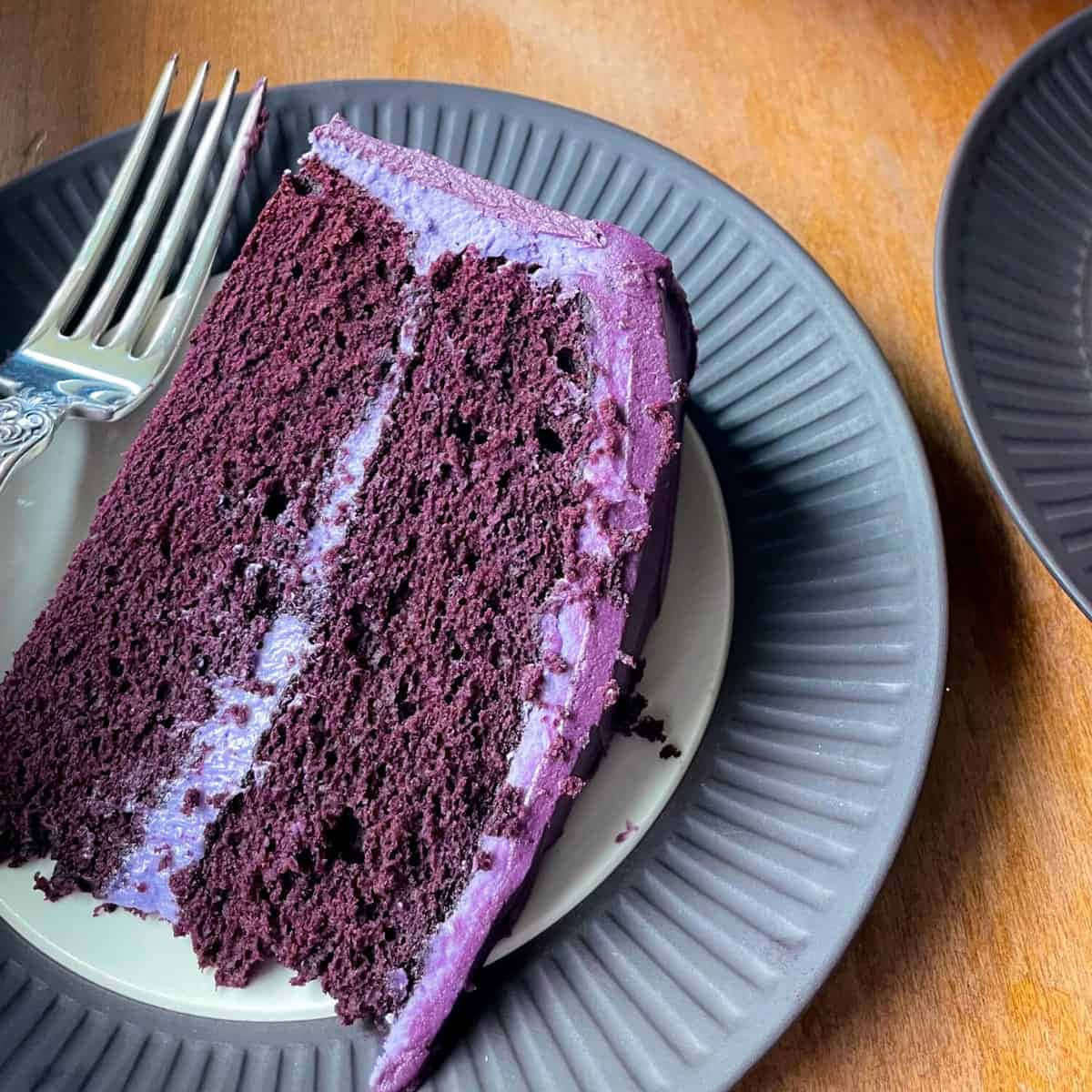 Purple Velvet 桌布 壁紙 — 一片濃郁的紫色天鵝絨蛋糕，配上相配的糖霜，放在灰色有紋的盤子上，旁邊有一把銀叉。