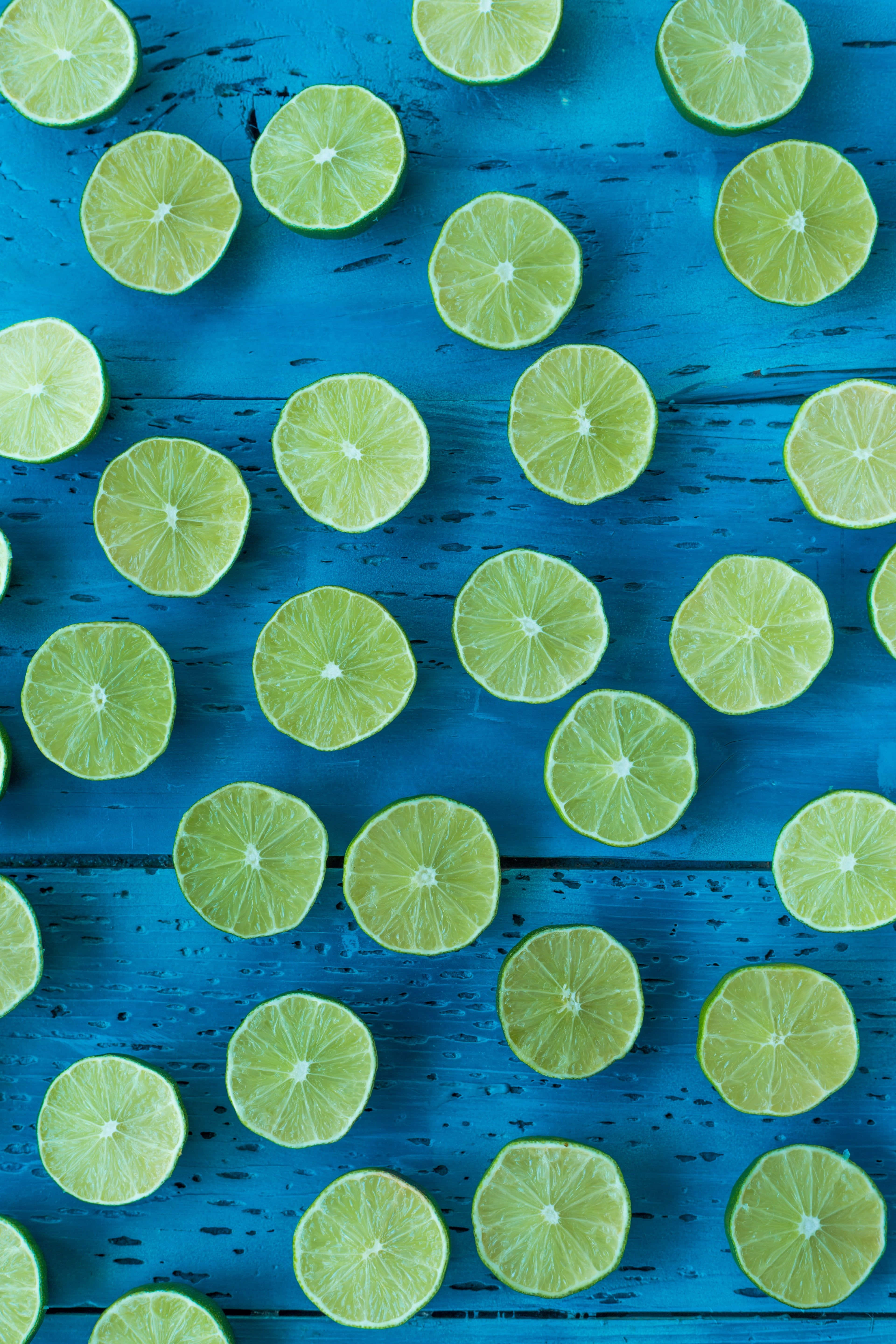 Lime 桌布 壁紙 — 切片萊姆排列在有紋理的藍色木質表面上，構成充滿活力的俯視構圖。
