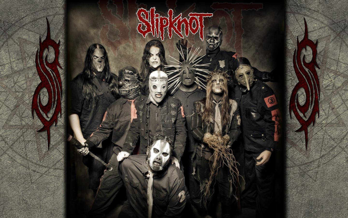 Slipknot 桌布 壁紙 — Slipknot 樂團成員戴著怪誕面具，在帶有紅色部落標誌的破裂混凝土背景下強烈擺姿勢。
